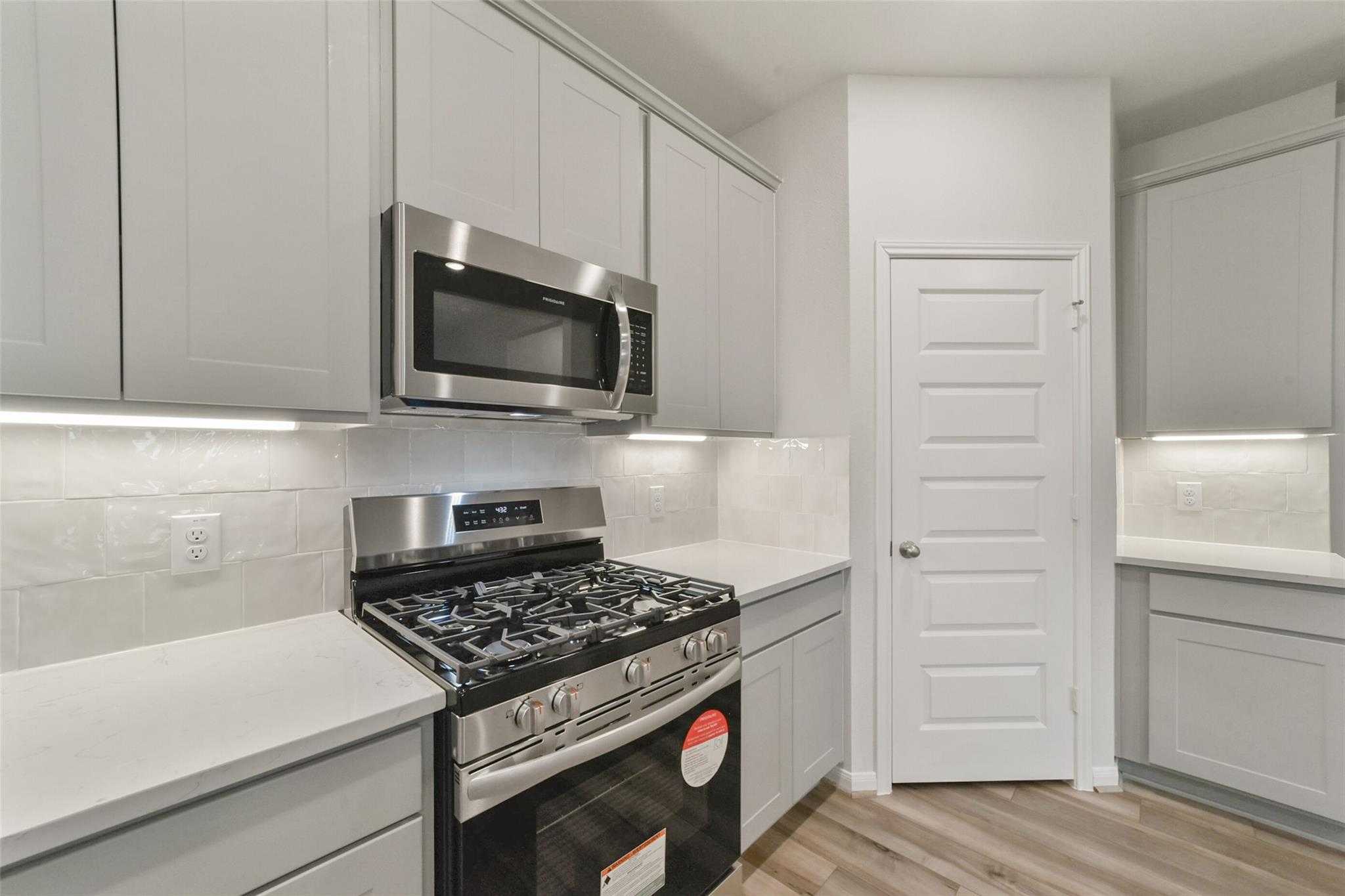 Modern kitchen with white shaker cabinets, stainless steel gas range and microwave in Davidson Homes San Marcos E, Beasley, TX