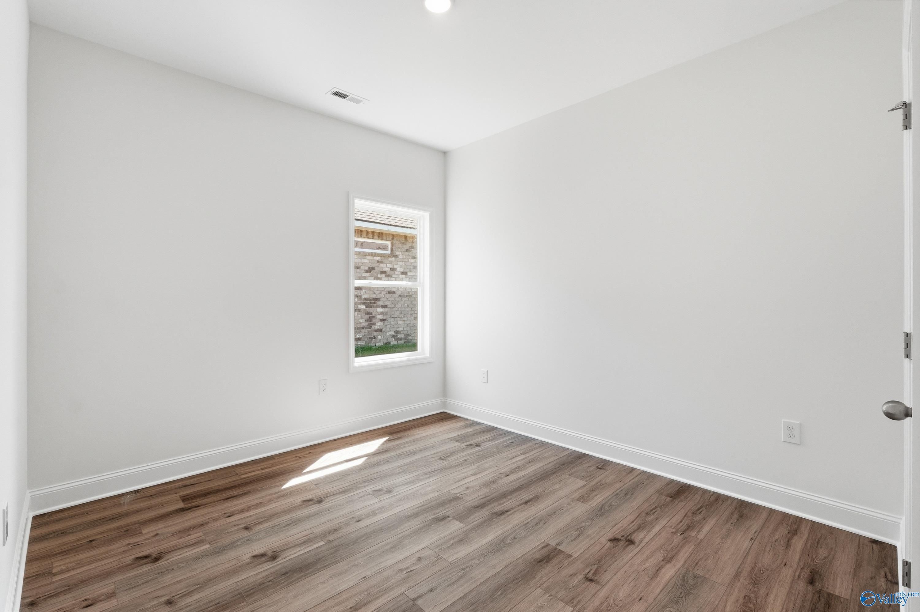 Bright bedroom with wood-look flooring and white walls in The Asheville floor plan at Jaguar Hills, Huntsville, Alabama.