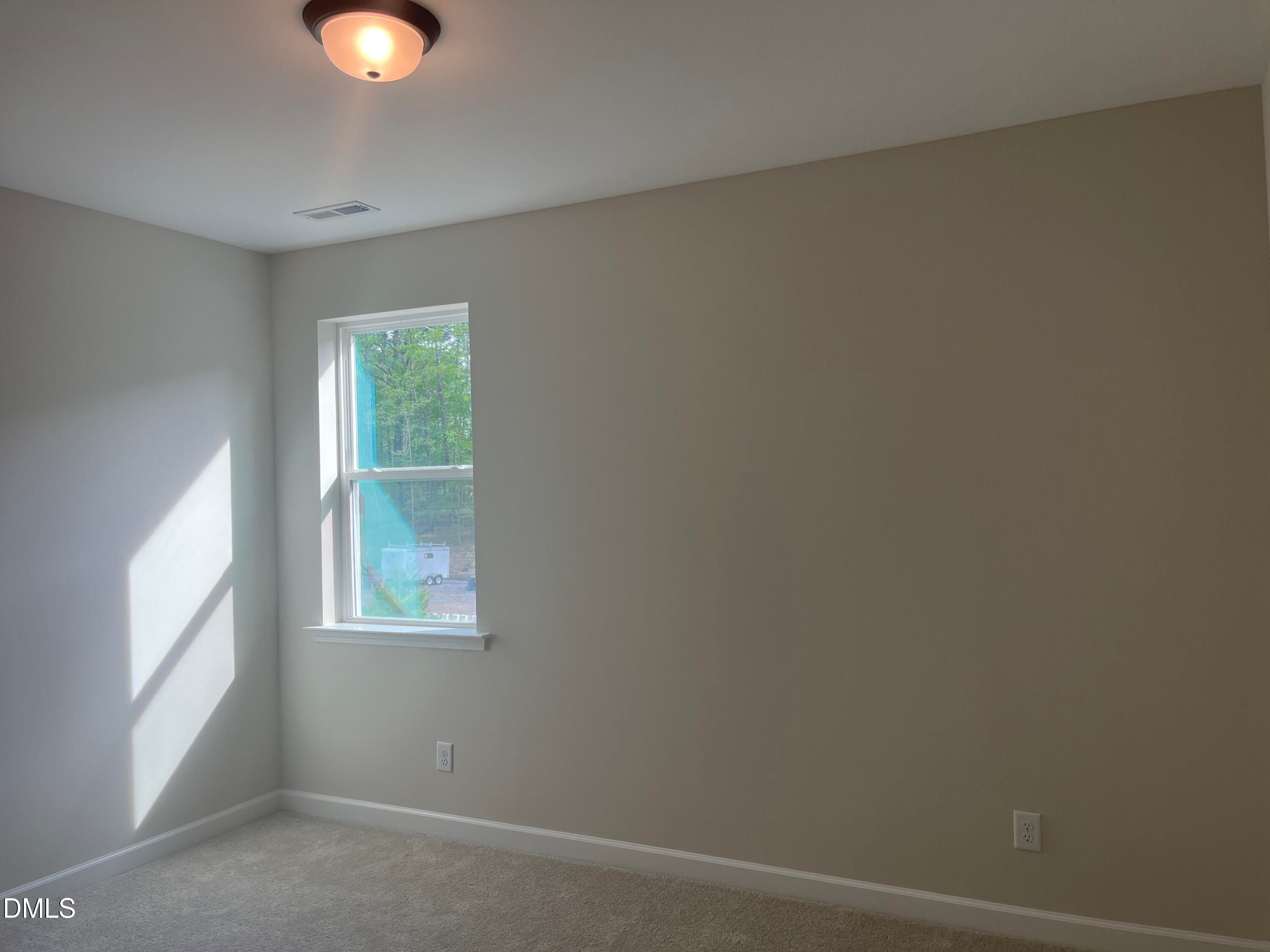 Bright empty bedroom featuring beige walls, carpet floor, and sunlit window with tree view in Davidson Homes Ashport L, Wake Forest, NC