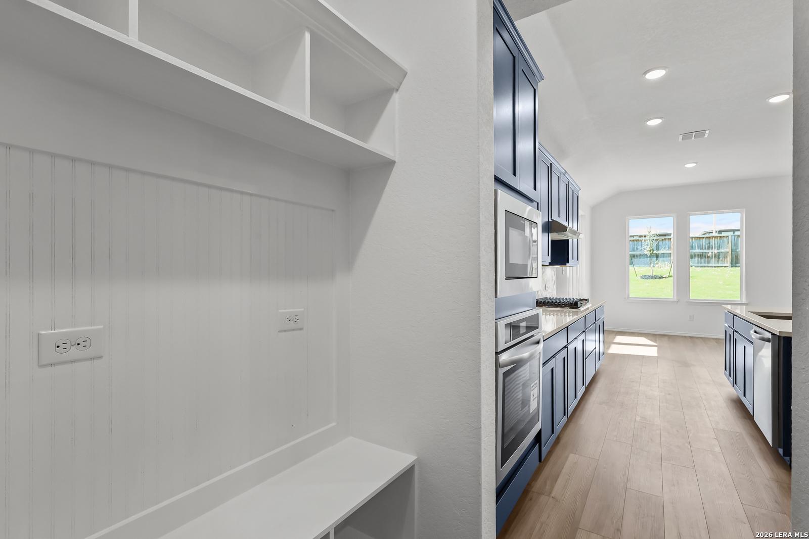 Mudroom with white shiplap walls, built-in bench and shelves beside navy cabinet kitchen in Davidson Homes The Sequoia B, San Antonio
