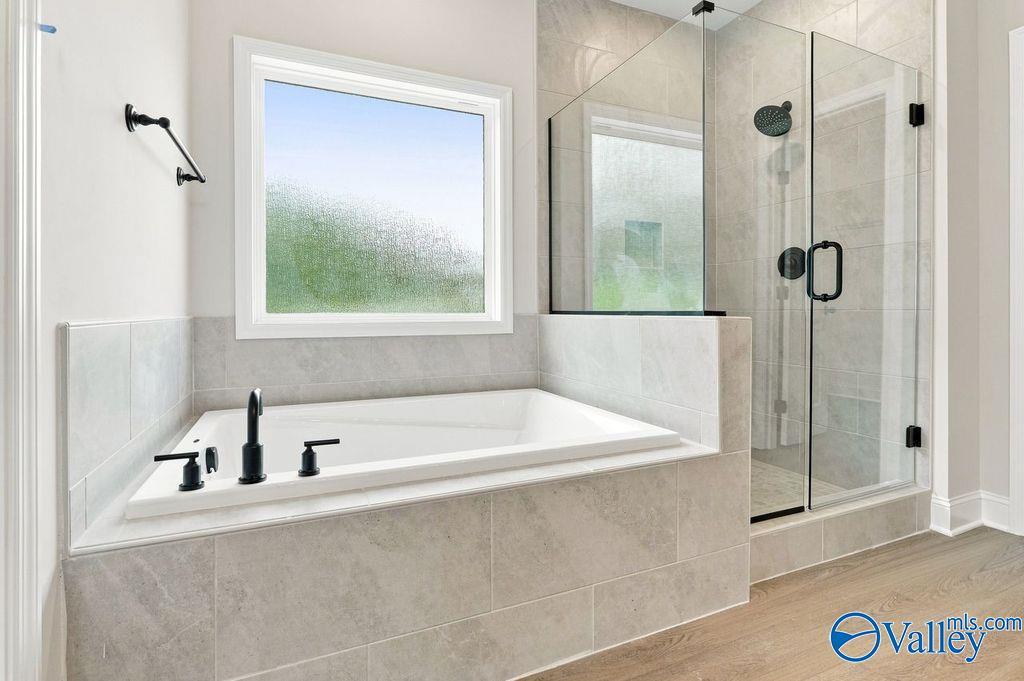 Soaking tub with matte black fixtures beside glass walk-in shower in master bath of Davidson Homes Rockford plan, Hartselle, AL