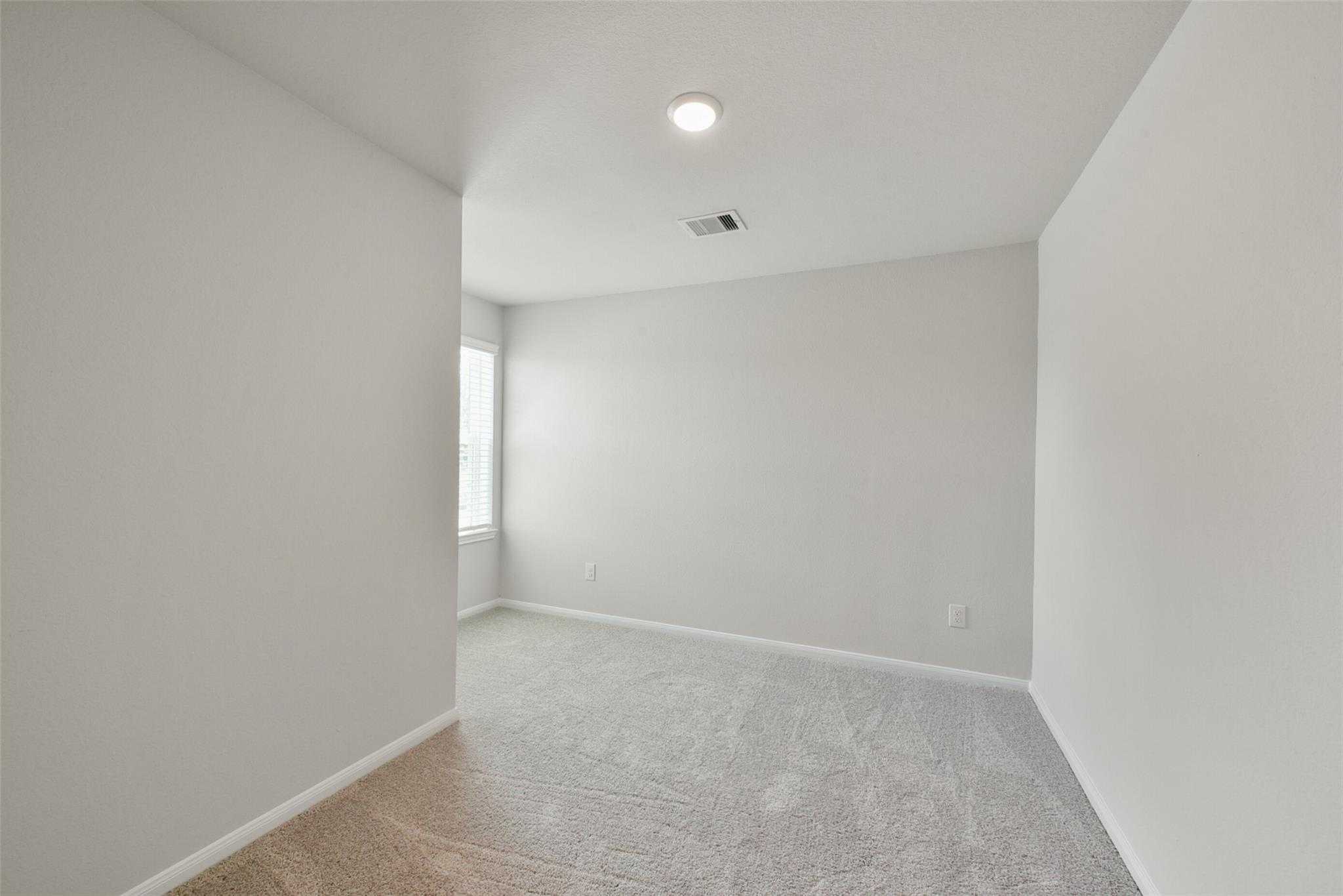 Spacious empty bedroom with light gray walls, plush carpet, and window in Davidson Homes The Sabine E, Dayton, Texas