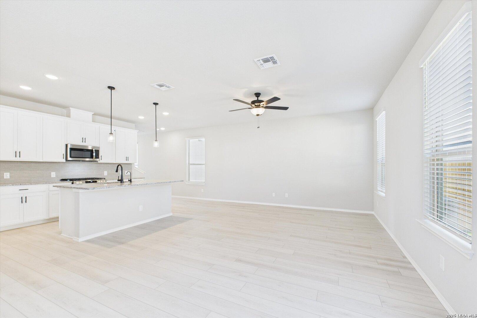 Modern open-concept kitchen with white cabinets, island, stainless appliances, and ceiling fan in The Charlotte A, San Antonio