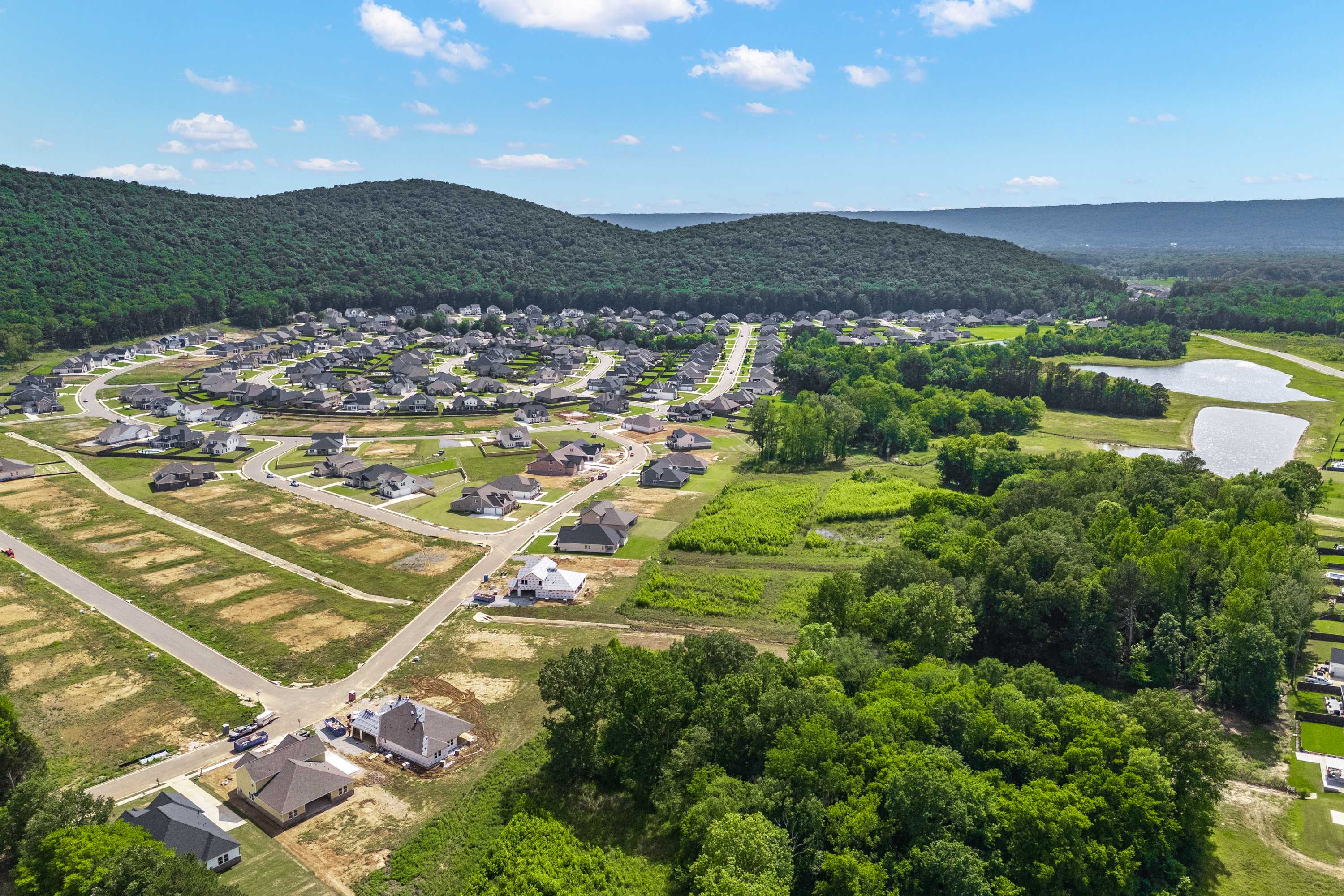 Aerial view of The Meadows at Hampton Cove in Owens Cross Roads AL featuring clustered homes wooded hills pond and green spaces