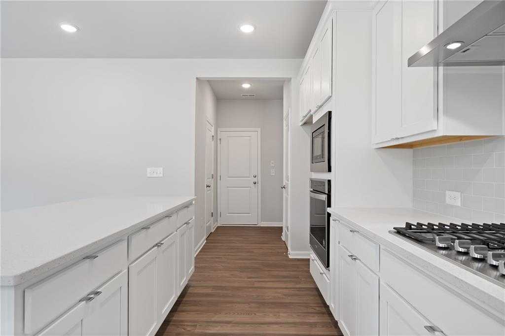 Modern white kitchen with shaker cabinets, quartz island, stainless double oven, gas range in The Hickory B by Davidson Homes, Winder, GA