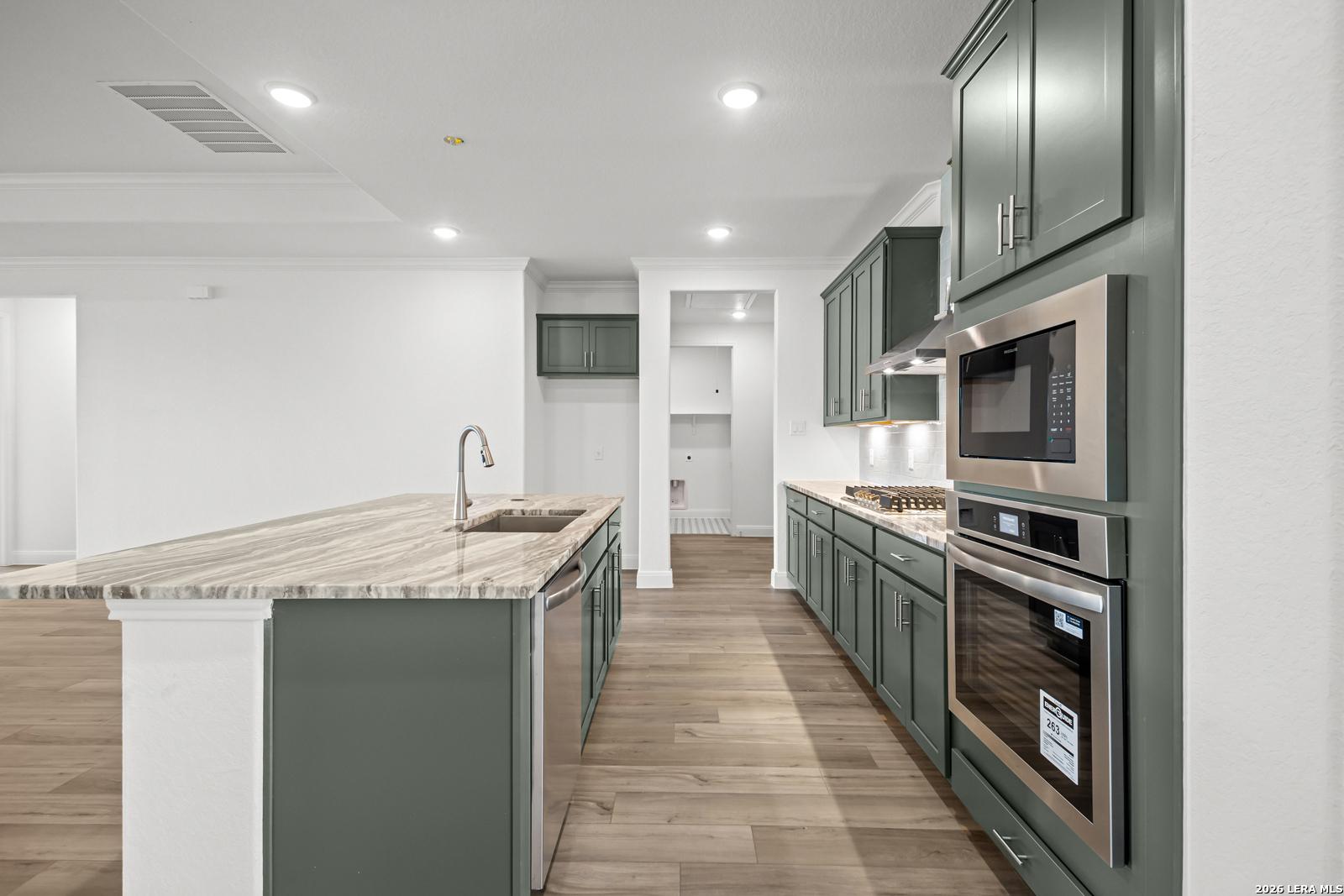 Modern kitchen with green cabinets, stone island, and stainless appliances in The Lanier G home, Castroville, Texas.