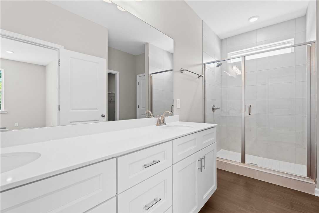 Elegant master bathroom with white double vanity, frameless glass shower, subway tile walls in Evermore Homes The Orion, Cusseta, Alabama