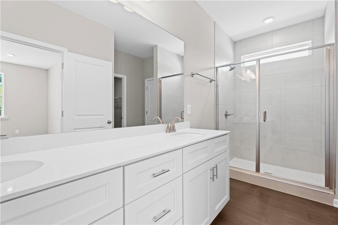 Modern master bathroom with white double vanity, frameless glass shower, and neutral tile in Evermore Homes The Orion, Cusseta, Alabama