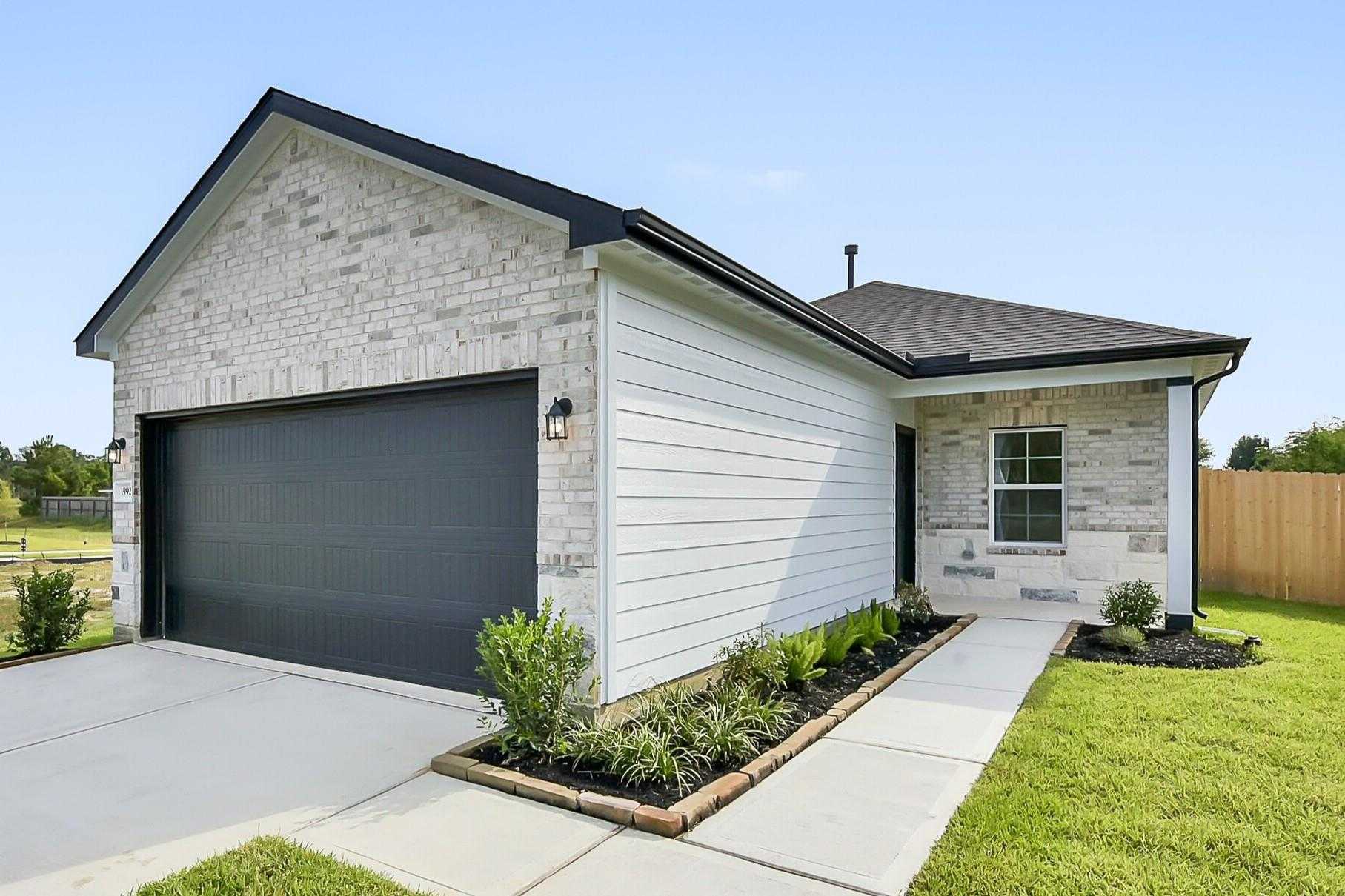 Modern 1-story Davidson Homes Comal G with white brick facade, black 2-car garage, and landscaped driveway in Dayton, Texas
