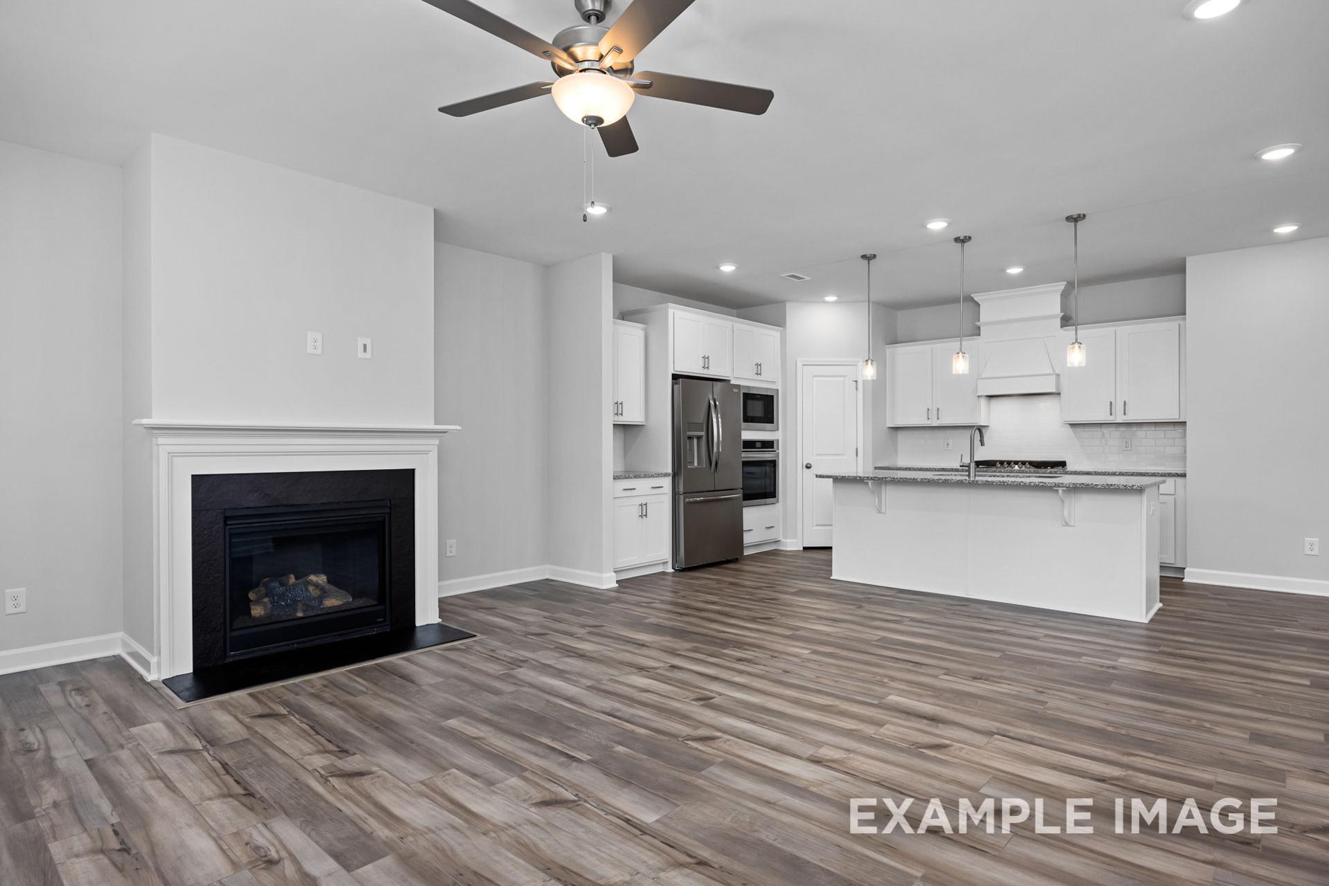 Open-concept living and kitchen in The Preston B, featuring white shaker cabinets, large island, stainless steel fridge, black gas fireplace, and light oak floors