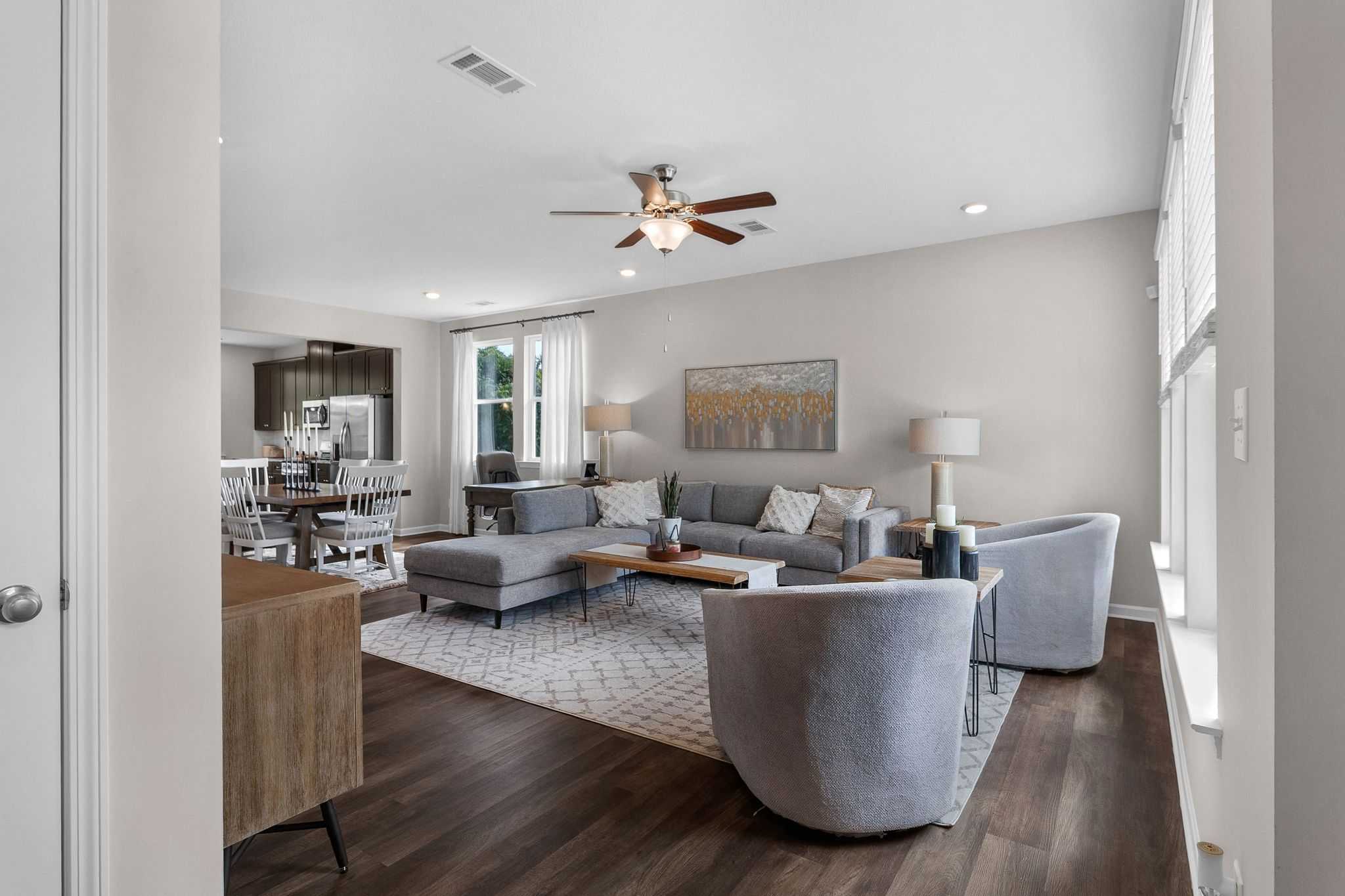 Spacious open-concept living room at Ivy Glen in Perry GA with gray sectional sofa, hardwood floors, ceiling fan, and adjacent kitchen