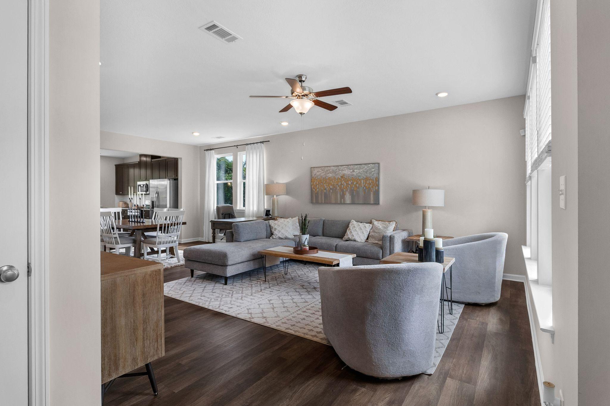 Spacious open-concept living room at Ivy Glen in Perry GA with gray sectional sofa, hardwood floors, ceiling fan, and adjacent kitchen