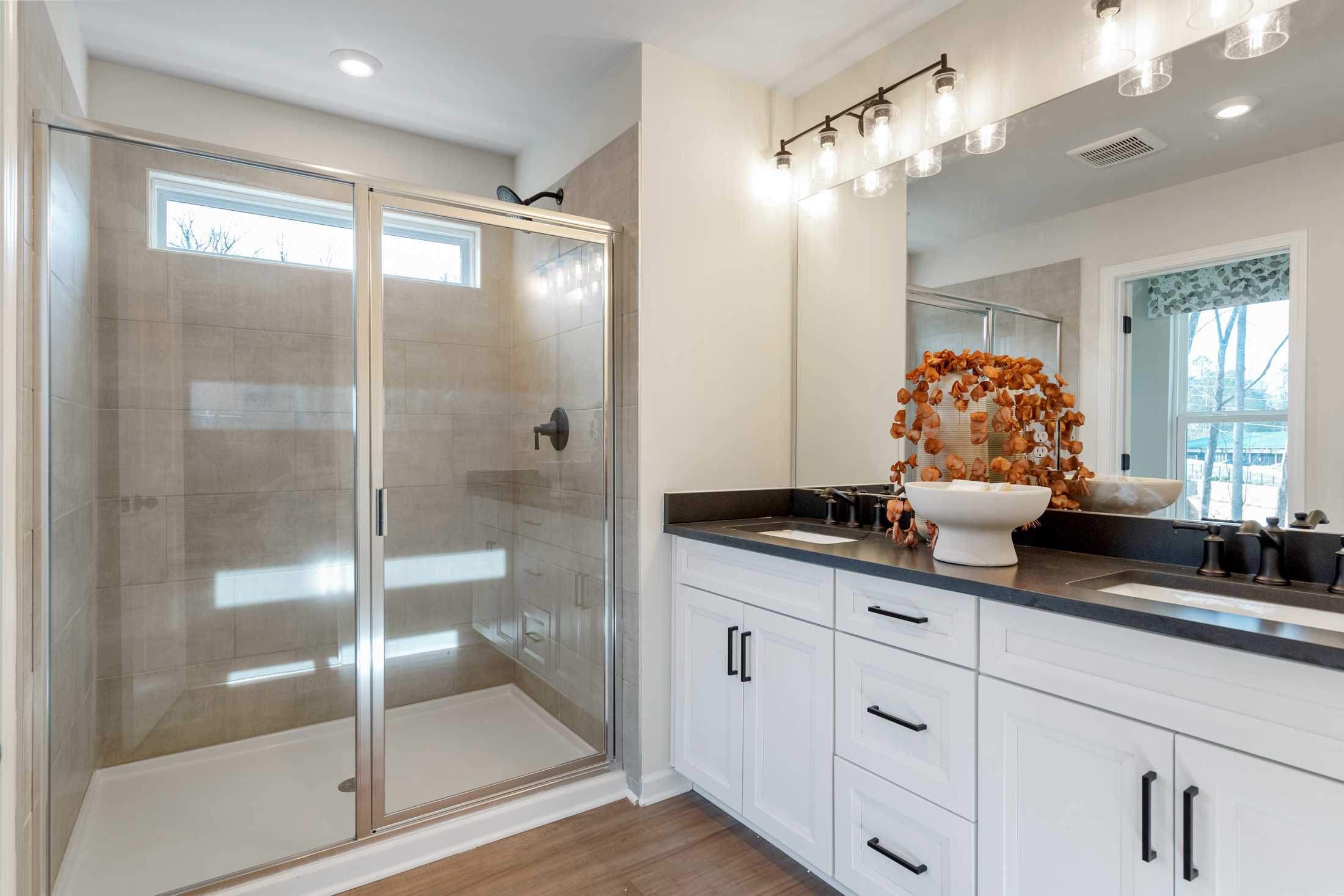 Spacious primary bathroom at Lake Shore in Winder GA with frameless glass shower, double white vanity, and hardwood floors