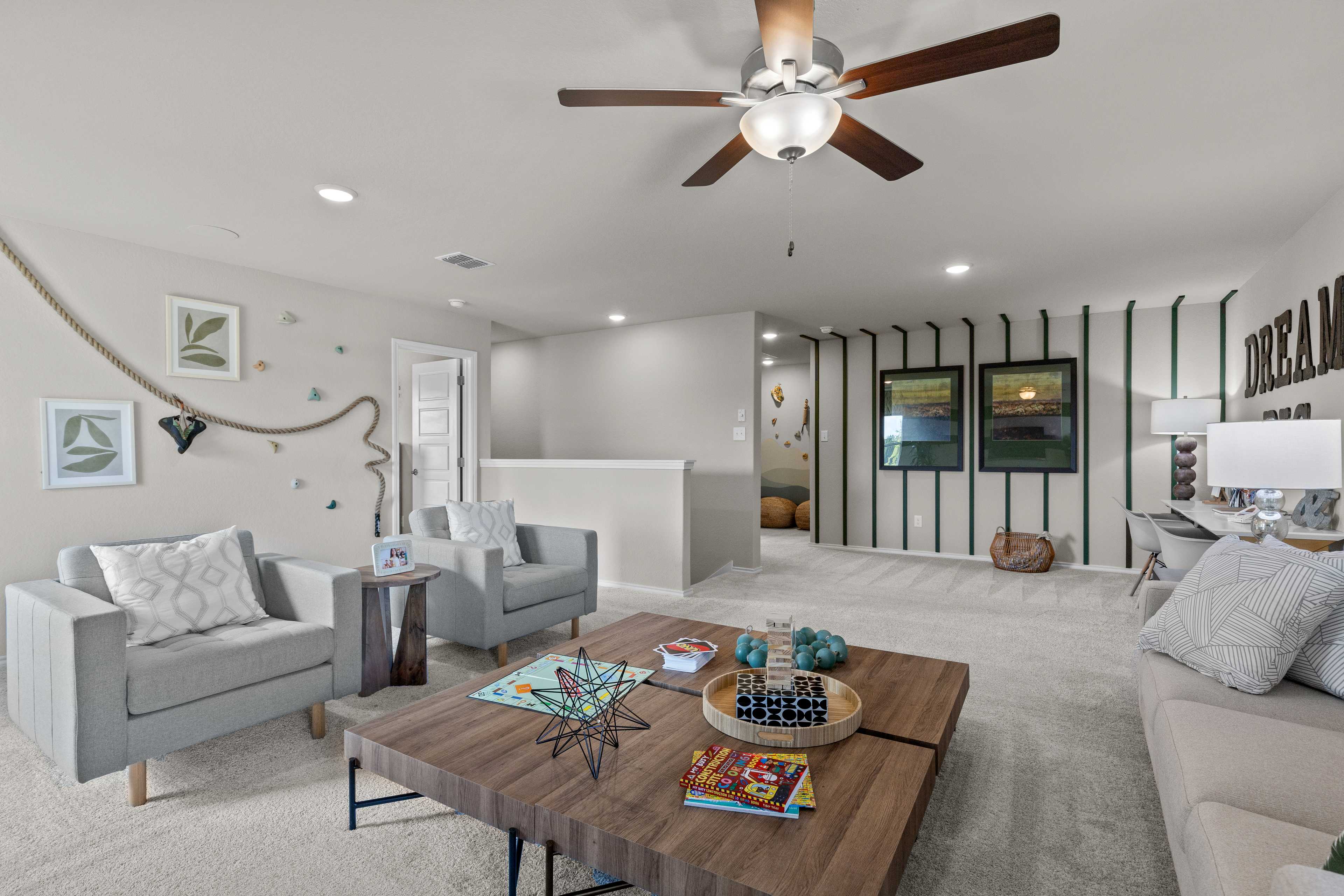 Cozy upstairs loft at Comanche Ridge in San Antonio TX with armchairs, sofa, wooden coffee table, striped accent wall, and ceiling fan