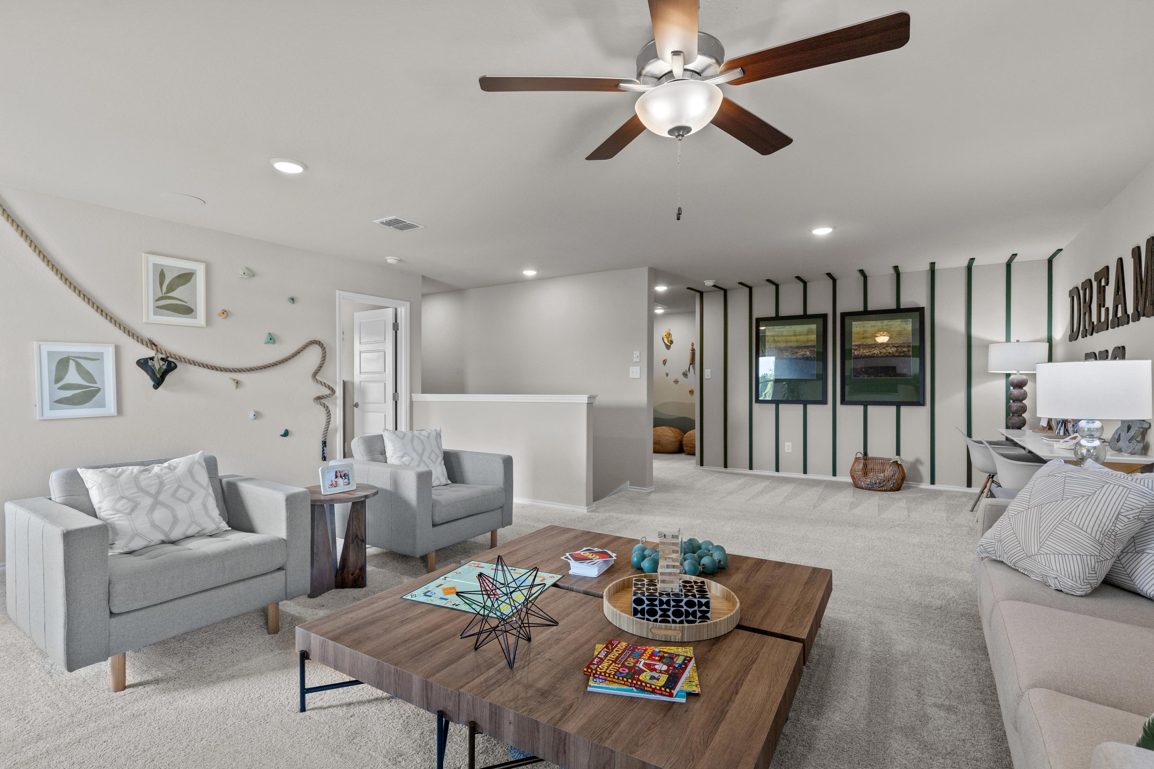 Cozy upstairs loft at Comanche Ridge in San Antonio TX with armchairs, sofa, wooden coffee table, striped accent wall, and ceiling fan