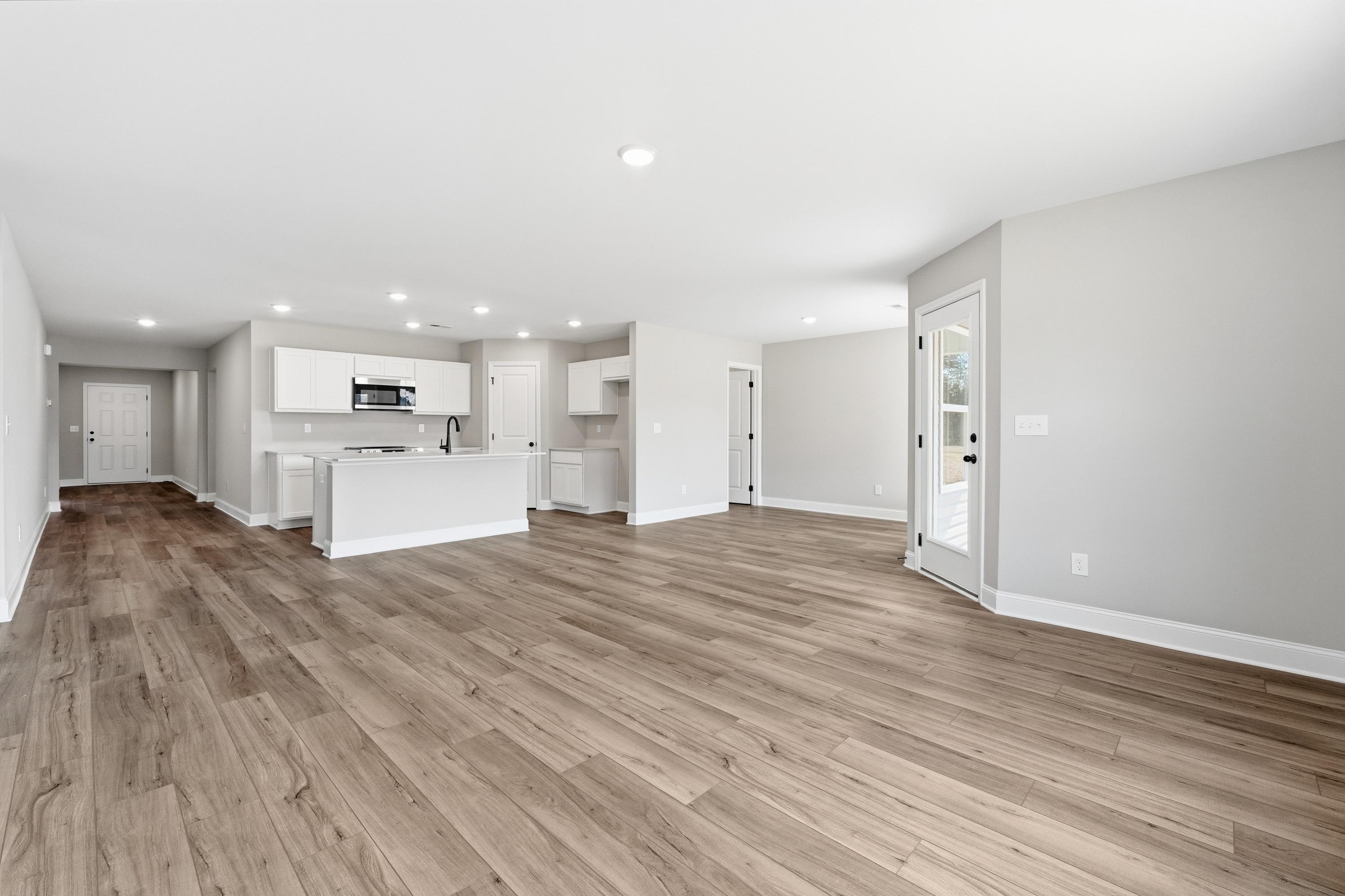Open-concept kitchen in The Daphne V with white cabinetry, large island, stainless appliances, hardwood floors, and French doors