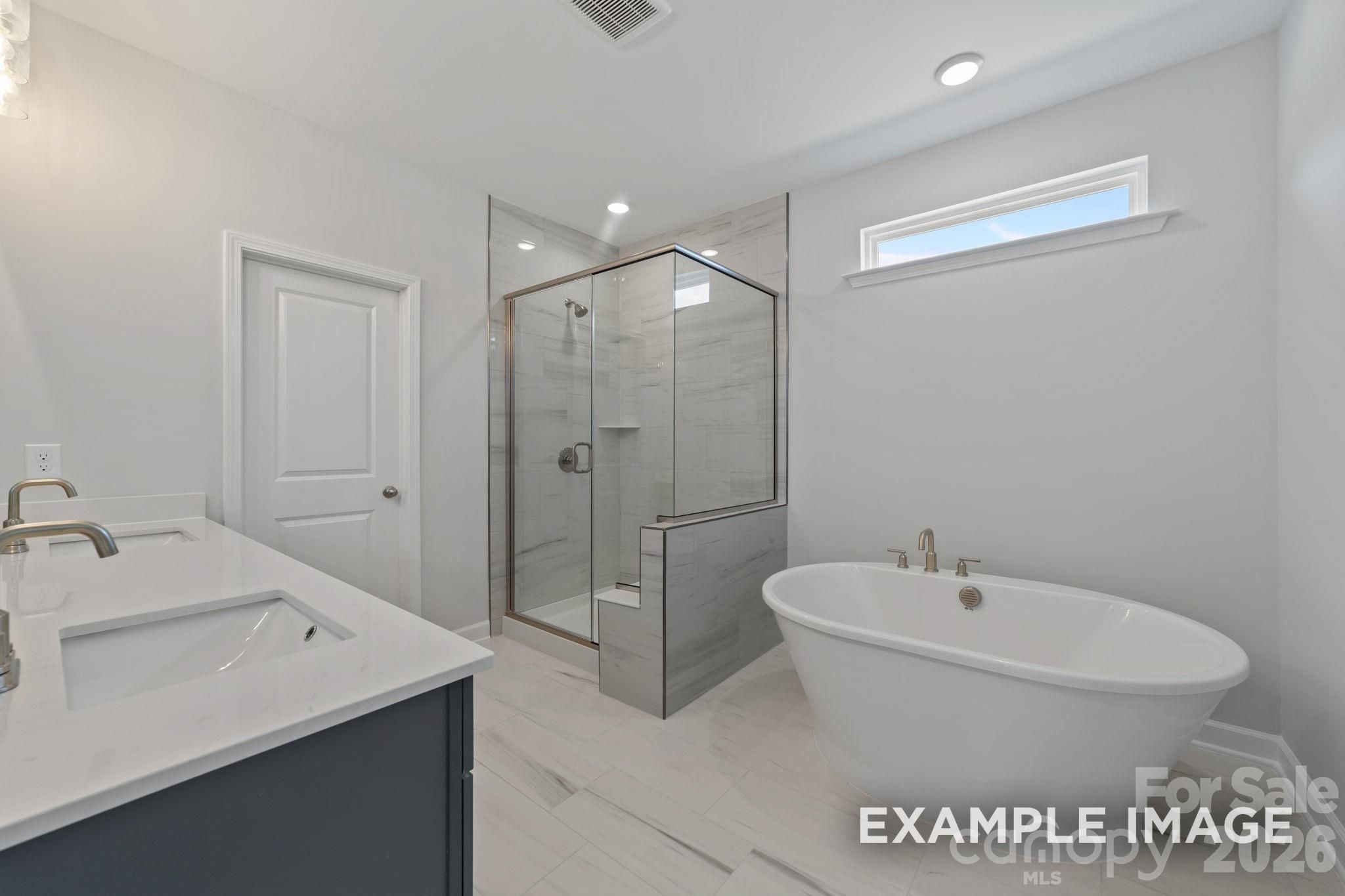 Modern primary bathroom with freestanding tub and glass-enclosed shower in The Magnolia B home in Windgate, Mooresville.