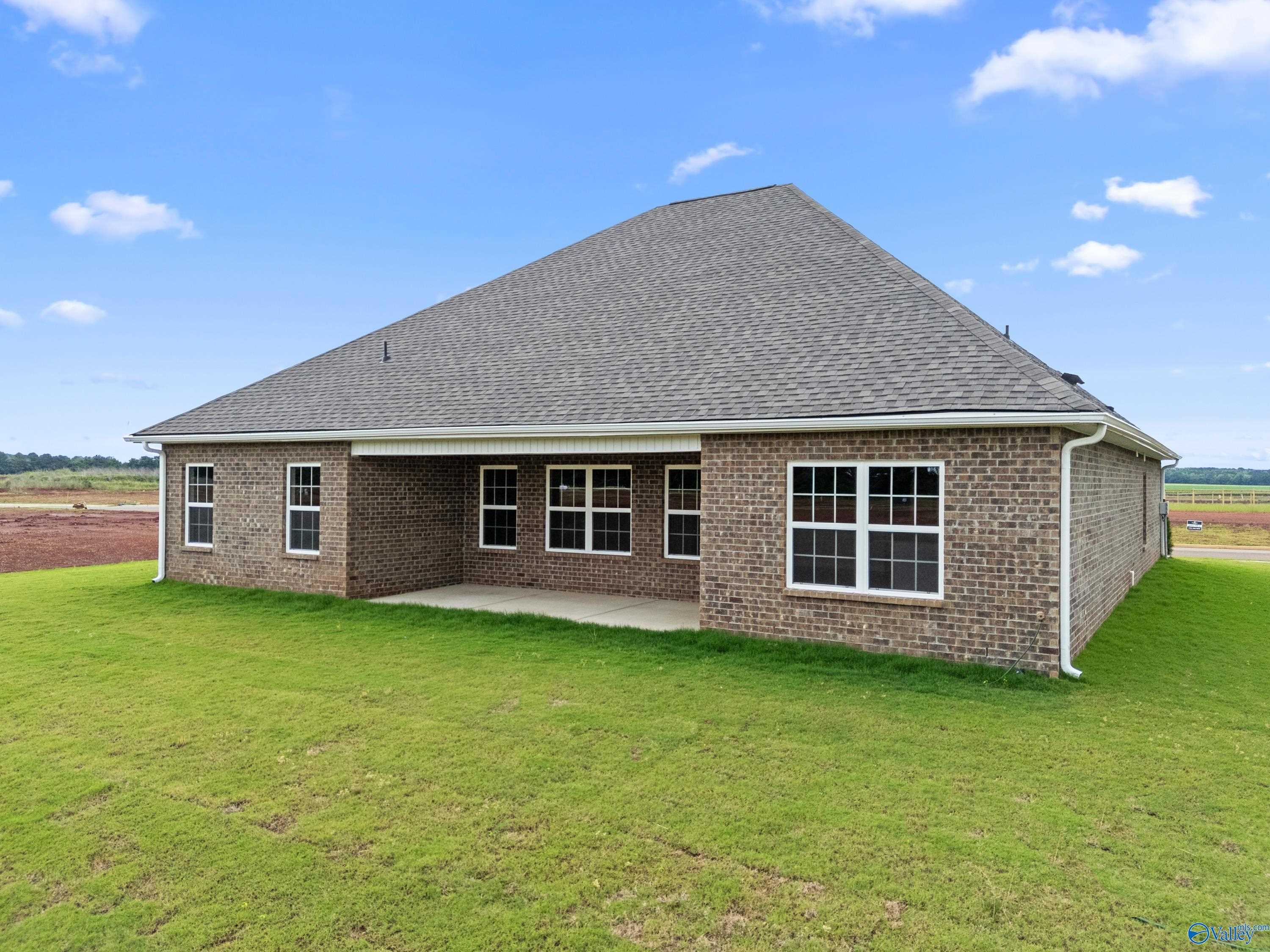 Rear view of brick single-story Davidson Homes Rockford B with Bonus: covered patio, large windows, lush green yard in Kendall Farms, Toney, Alabama