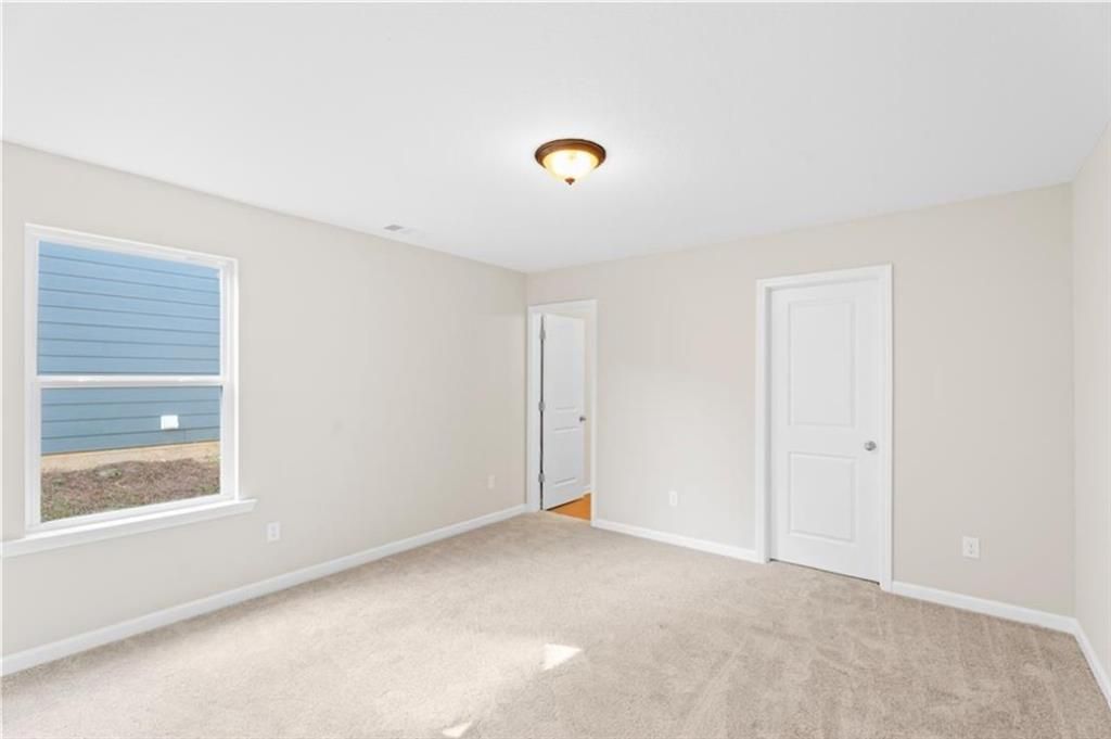 Bright secondary bedroom featuring beige walls, neutral carpet, window view, and interior door in Davidson Homes The Washington, Phenix City