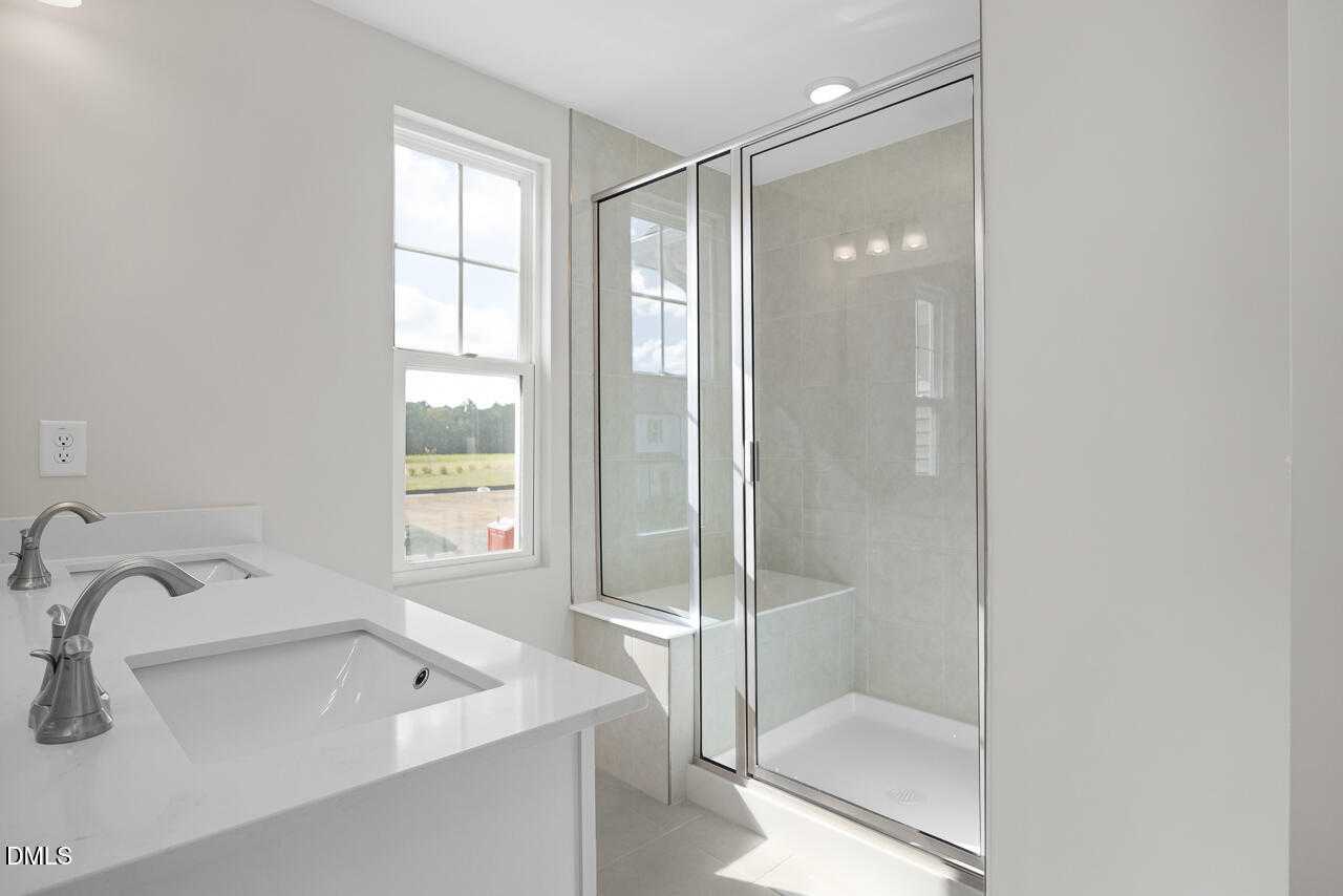 Modern master bathroom with double vanity, frameless glass shower, and window view in Davidson Homes The Warren, Fuquay-Varina, NC