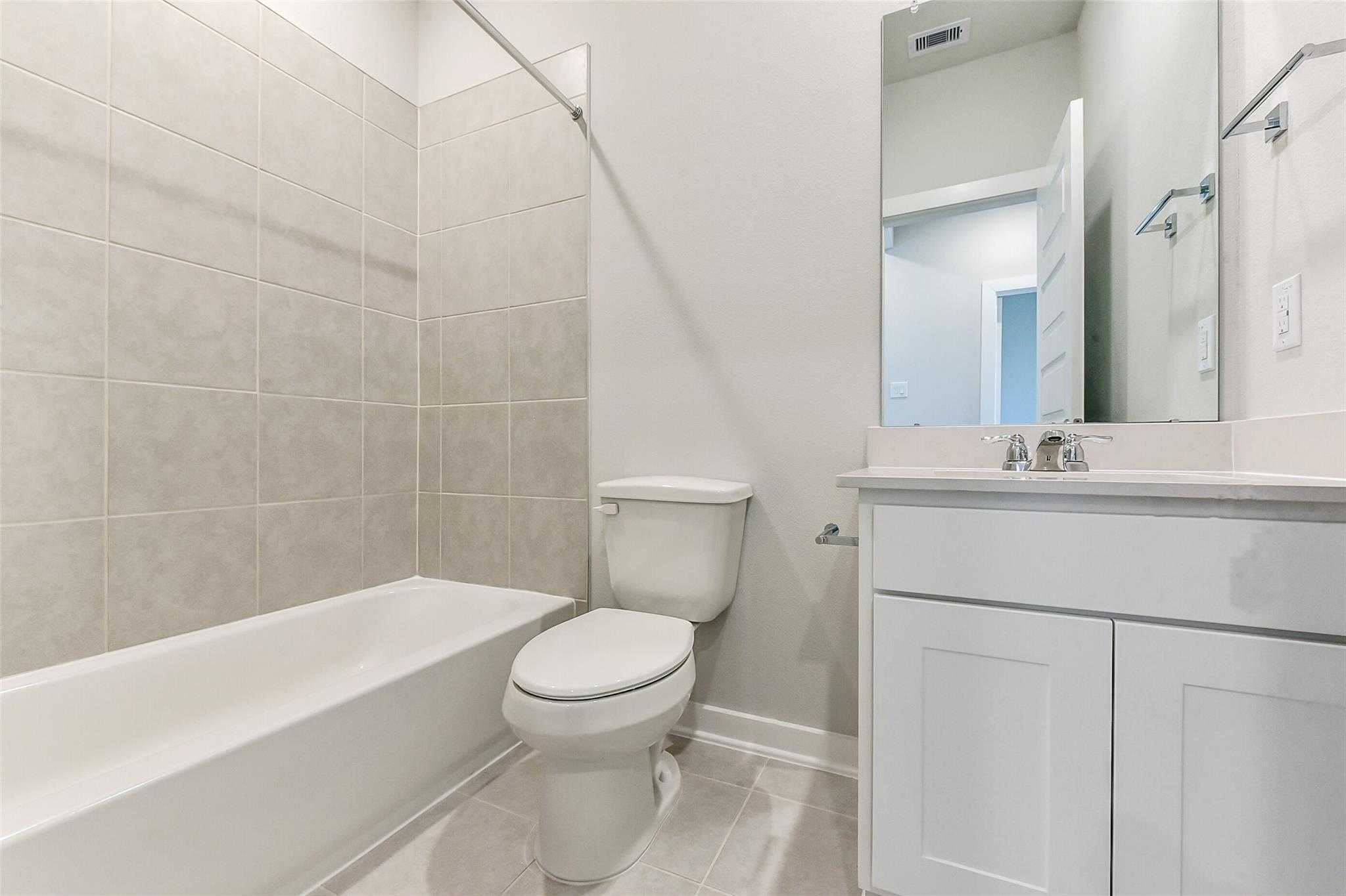 Modern guest bathroom featuring bathtub-shower combo, white vanity, tiled walls in Davidson Homes The Frio F, Dayton, Texas