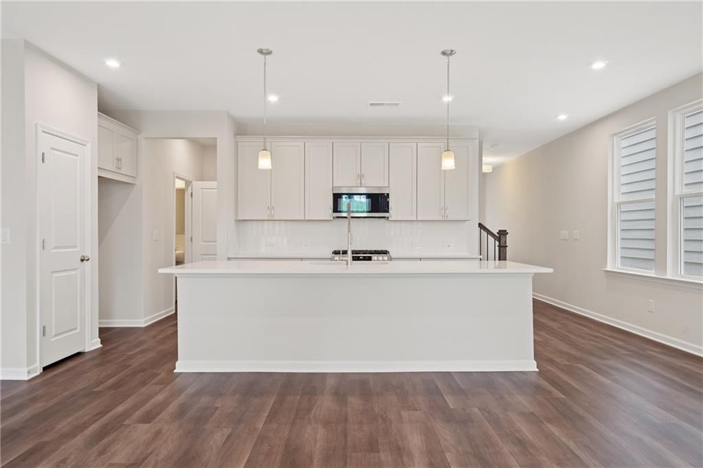 Modern white kitchen with large island, stainless appliances, and hardwood floors in The Cary B by Davidson Homes, Kennesaw, GA