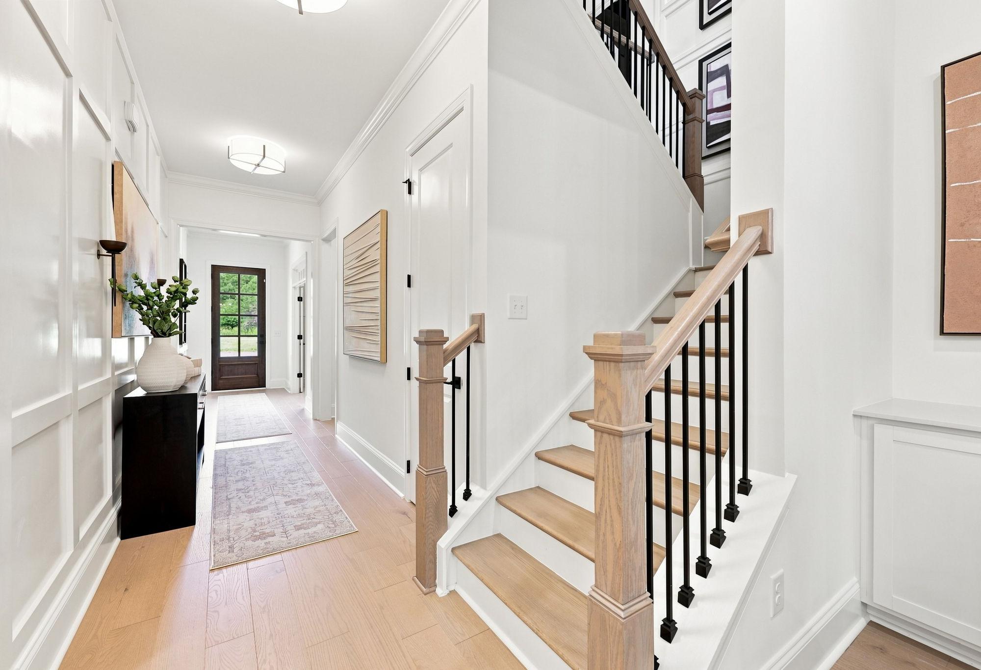 Bright foyer of The Barrington by Davidson Homes featuring a modern staircase with wooden handrails and paneled walls.