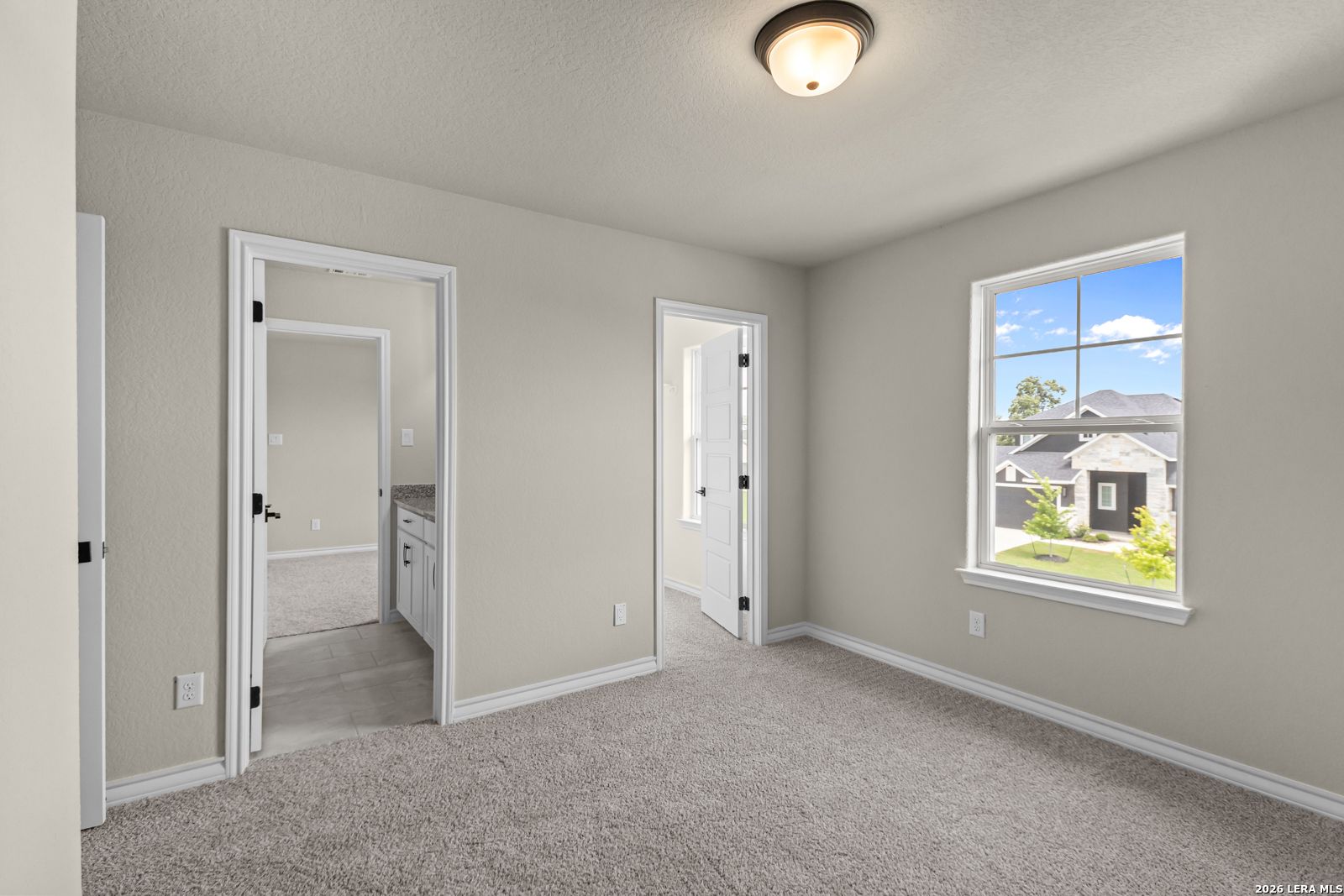 Neutral-toned bedroom with carpet, ensuite bathroom access, and large windows in The Danbury H, Castroville, Texas.