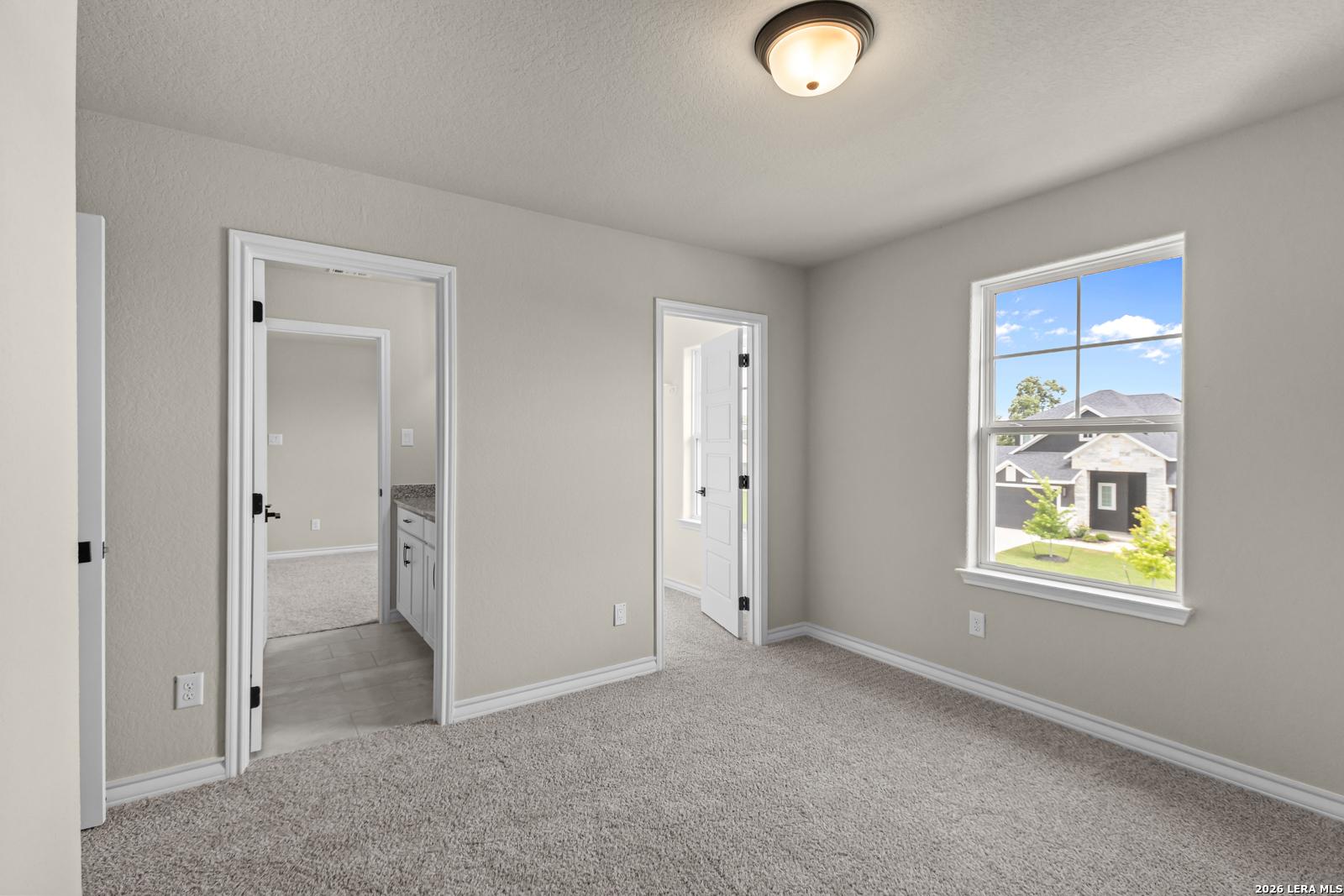 Neutral-toned bedroom with carpet, ensuite bathroom access, and large windows in The Danbury H, Castroville, Texas.