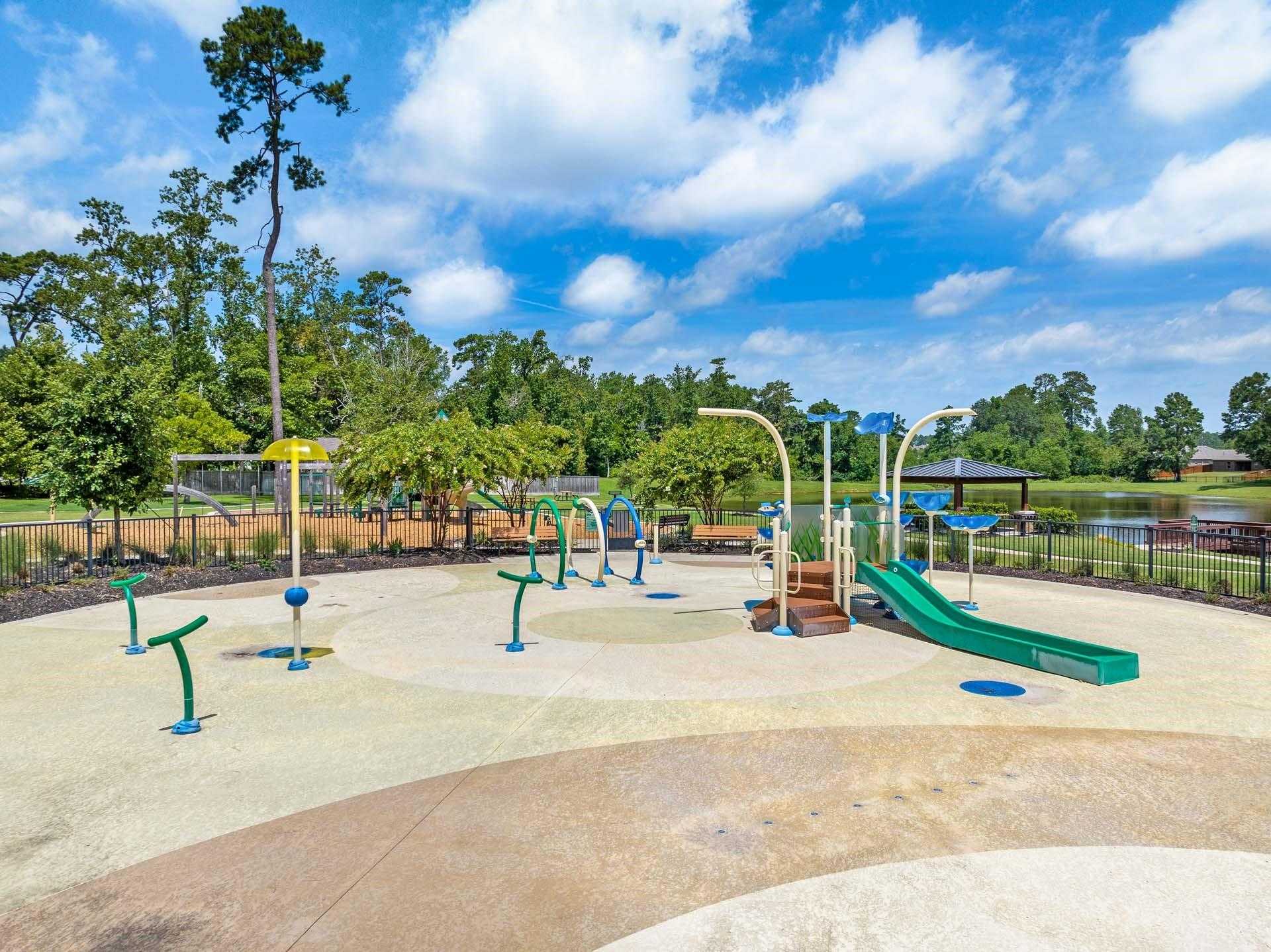 Vibrant splash pad playground with water spouts, green slide, hoops in Lakes at Black Oak, Magnolia, Texas