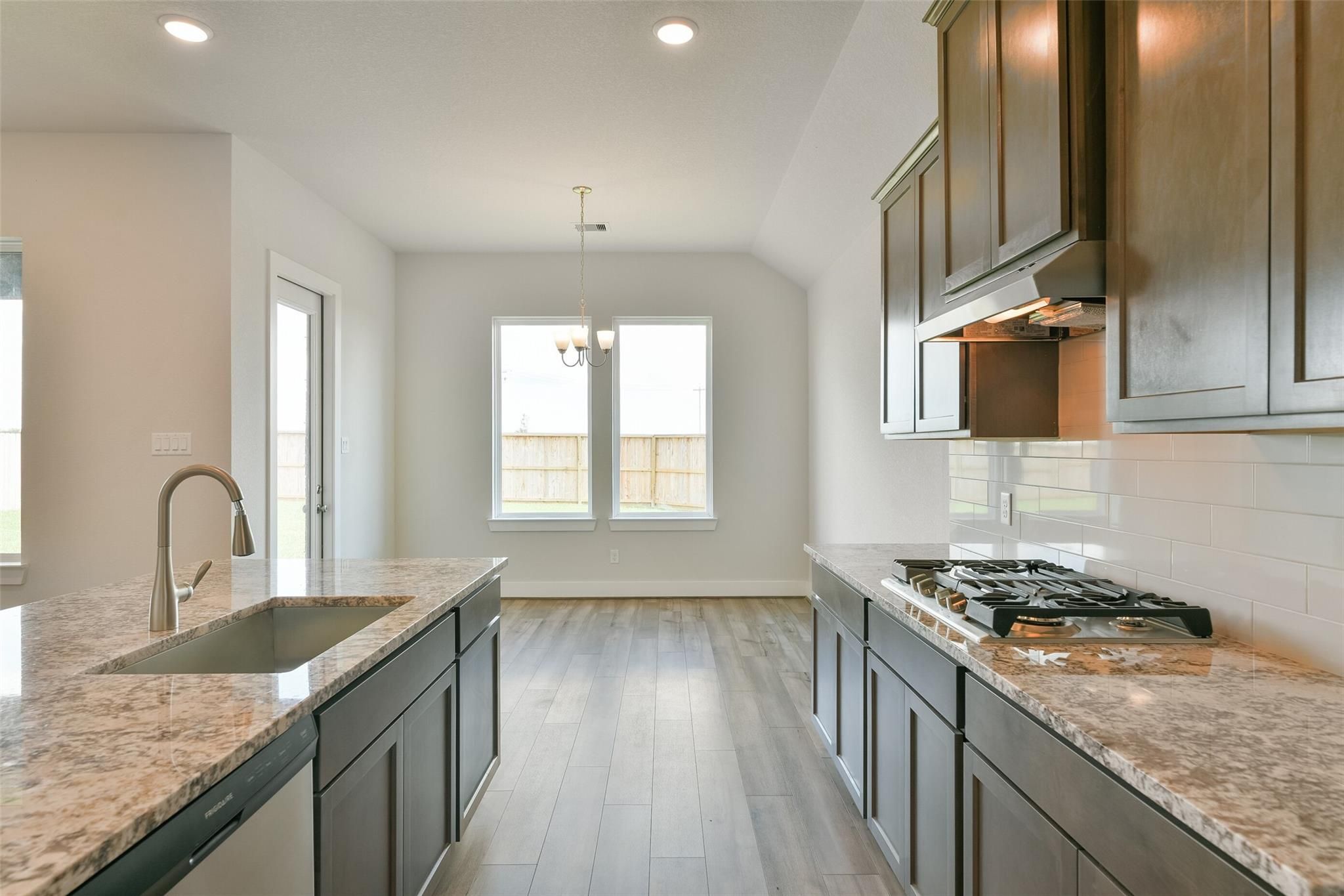 Modern open-concept kitchen with quartz countertops, dark shaker cabinets, gas range, and island sink in Davidson Homes The Edward A, Lago Mar