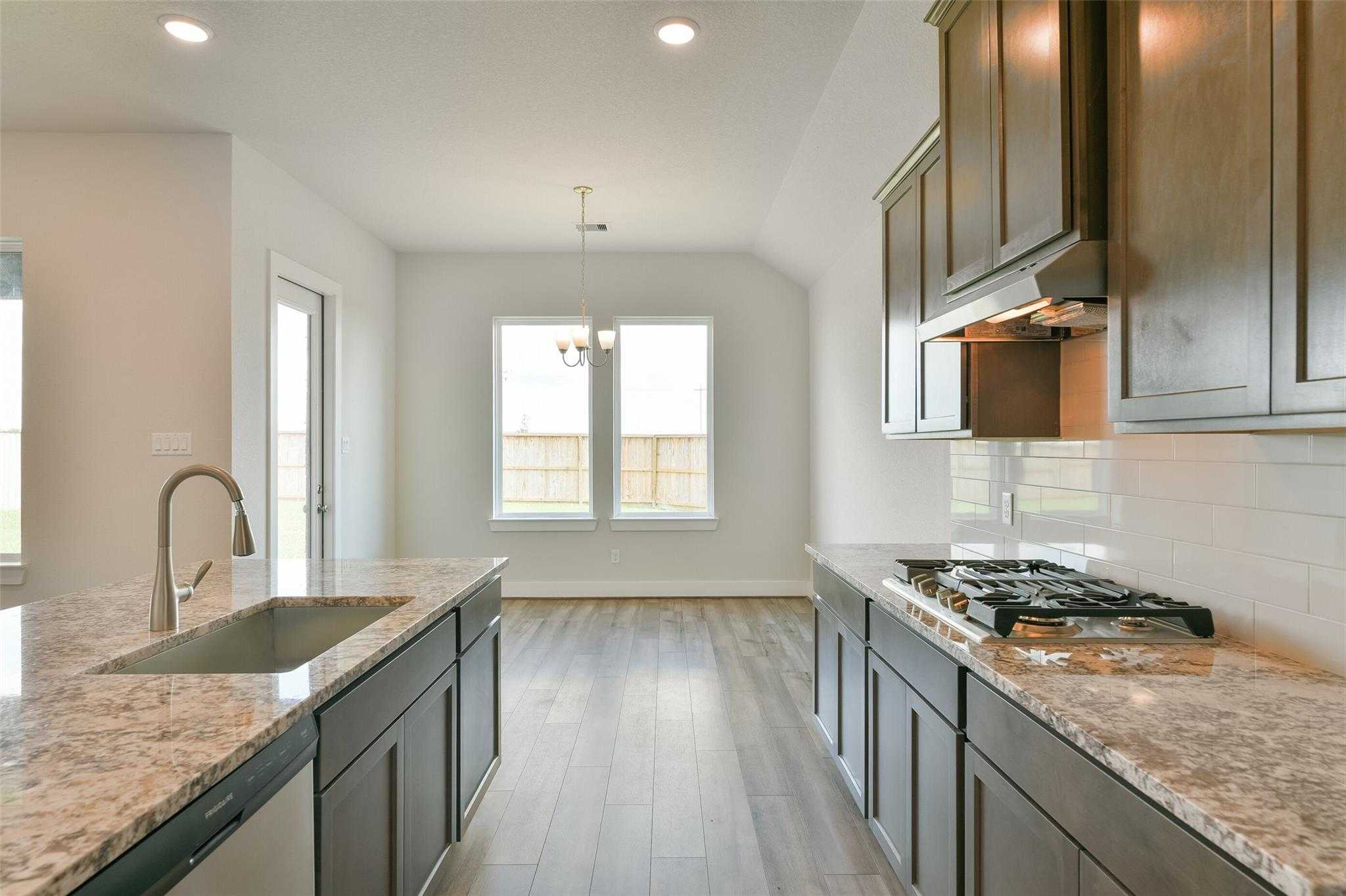 Modern open-concept kitchen with quartz countertops, dark shaker cabinets, gas range, and island sink in Davidson Homes The Edward A, Lago Mar