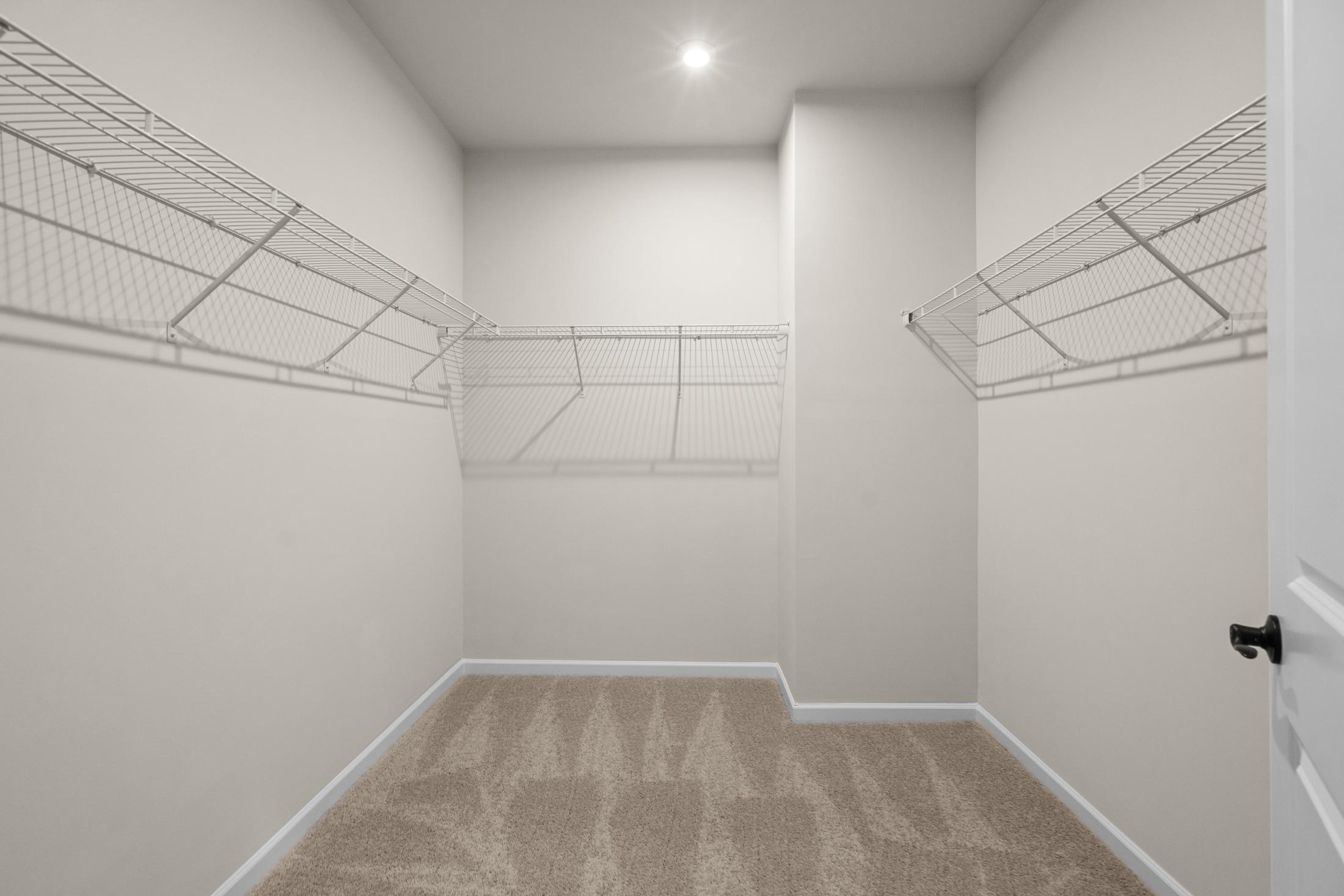 Spacious walk-in closet in The Glenwood master suite with wire shelving racks, beige walls, and carpeted floor