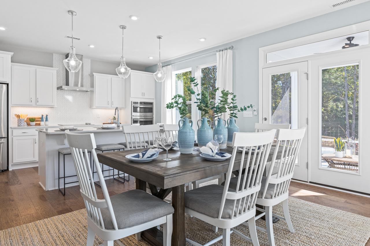 Open-concept dining and kitchen area in The Hemlock A featuring a farmhouse table, white cabinets, and modern island seating.