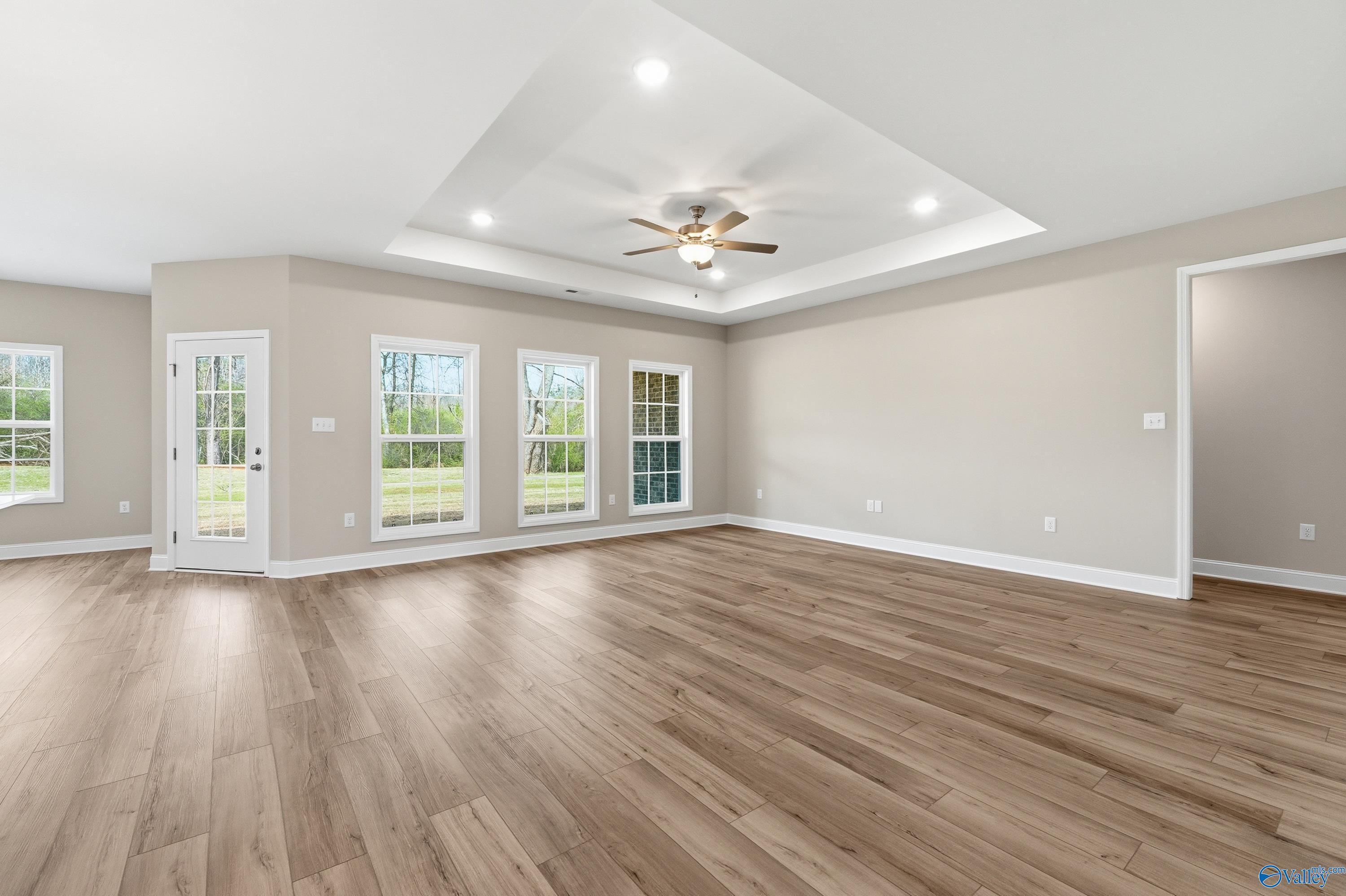 Spacious living room with hardwood floors, ceiling fan, large windows, and beige walls in The Harrison B by Davidson Homes, Decatur, AL