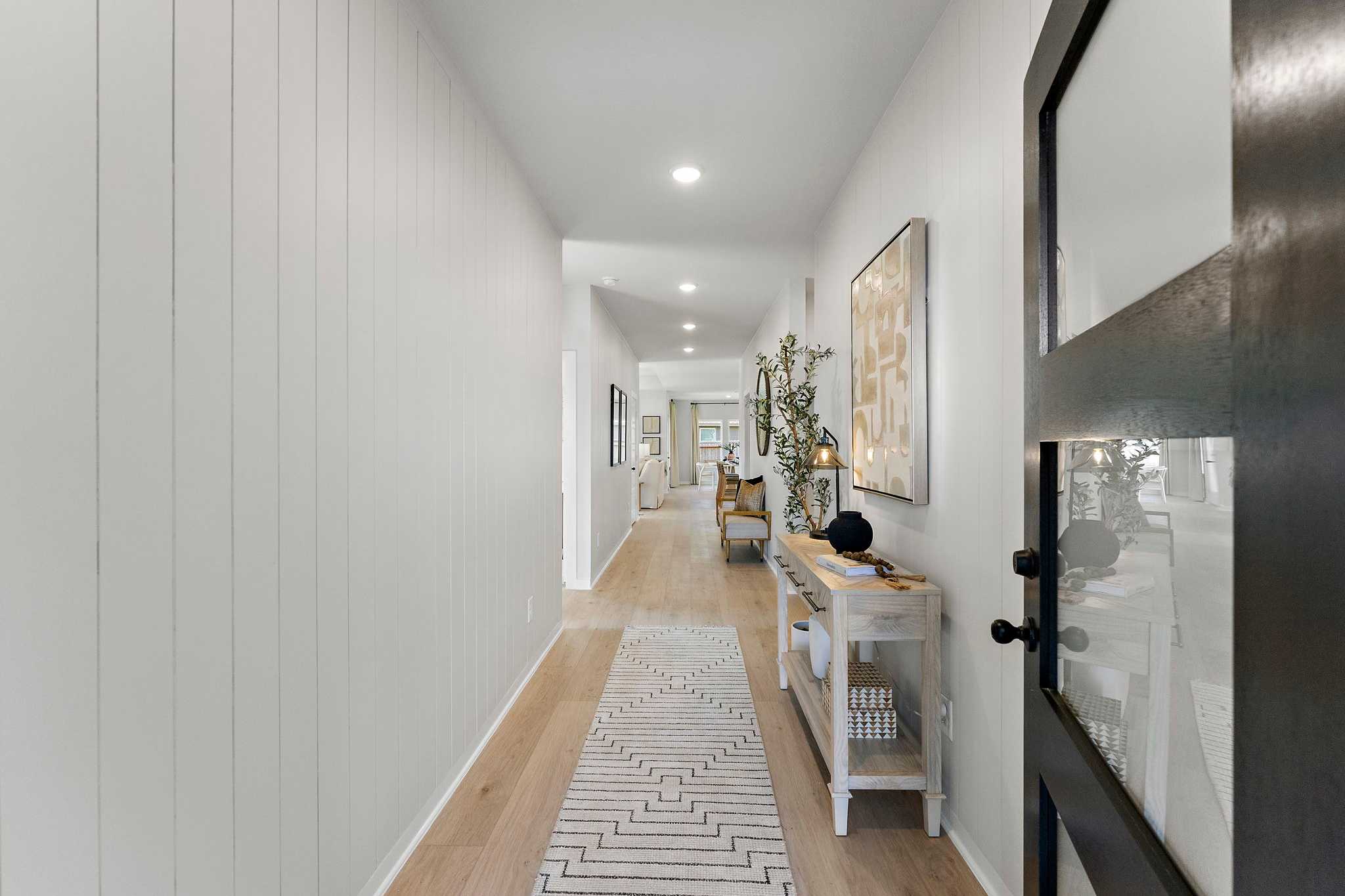 Spacious hallway with white shiplap walls, oak hardwood floors, patterned runner rug, and entry console at Sundance Cove in Crosby Texas