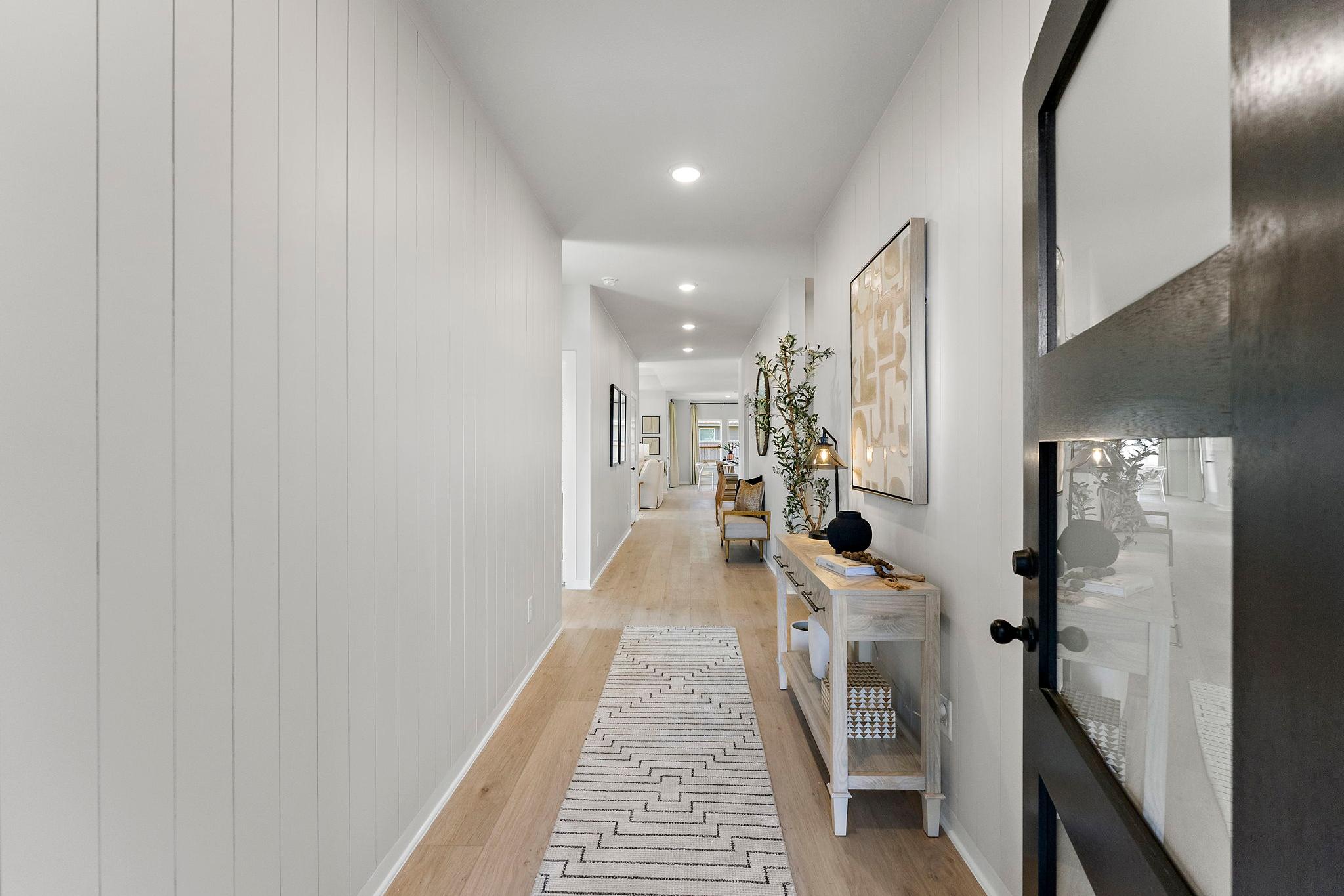 Spacious hallway with white shiplap walls, oak hardwood floors, patterned runner rug, and entry console at Sundance Cove in Crosby Texas