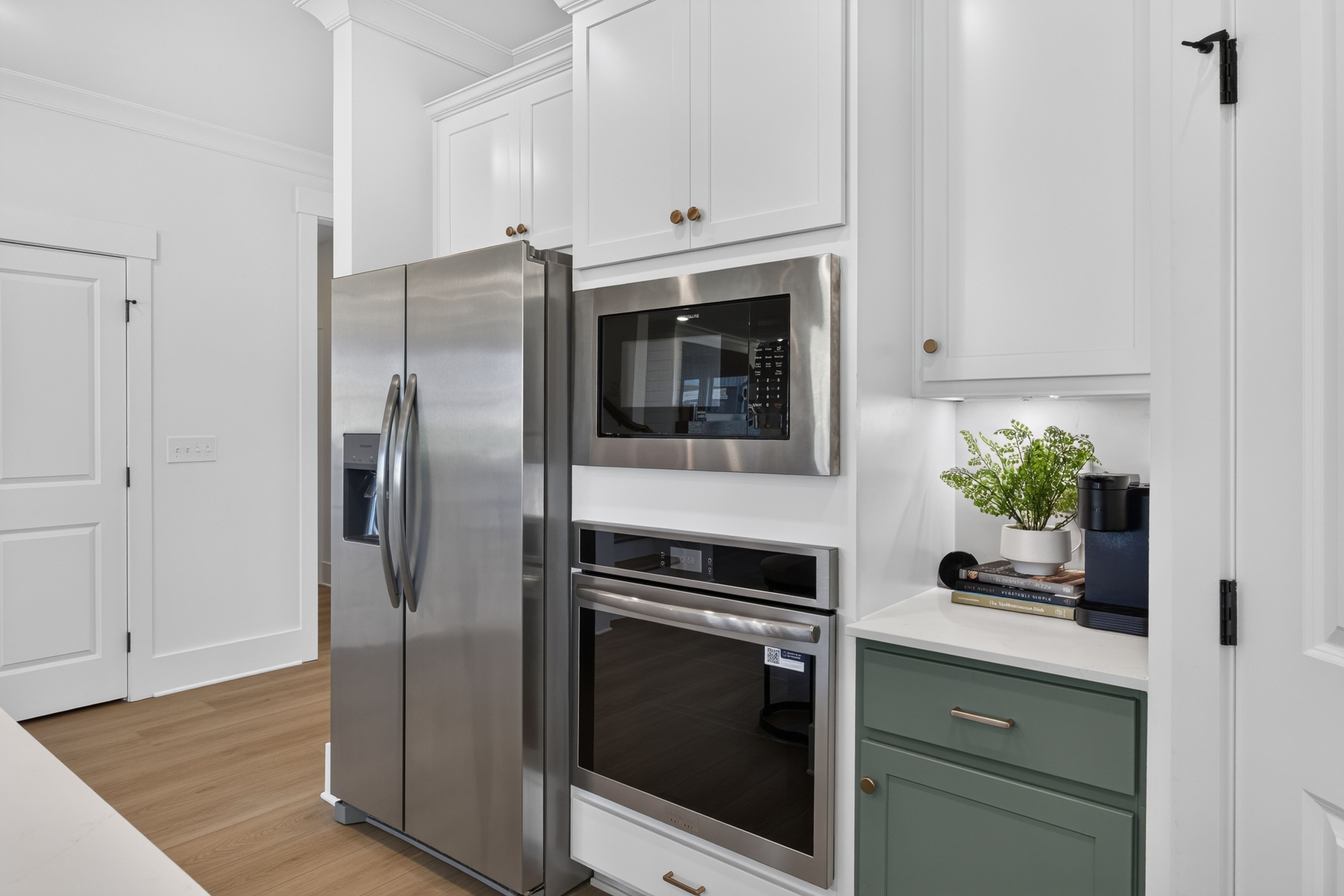 White kitchen with stainless steel appliances, built-in wall oven and microwave, sage green cabinetry at Evergreen Mill in Madison, AL