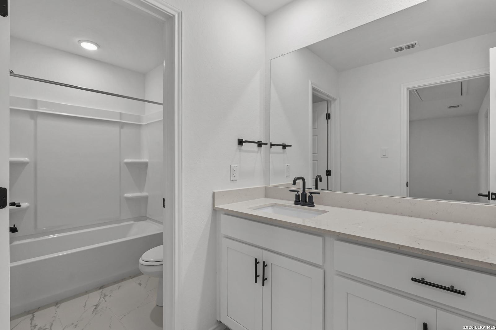 Modern bathroom with white vanity, quartz countertops, and tub-shower combo in The Gillian C by Davidson Homes, San Antonio.