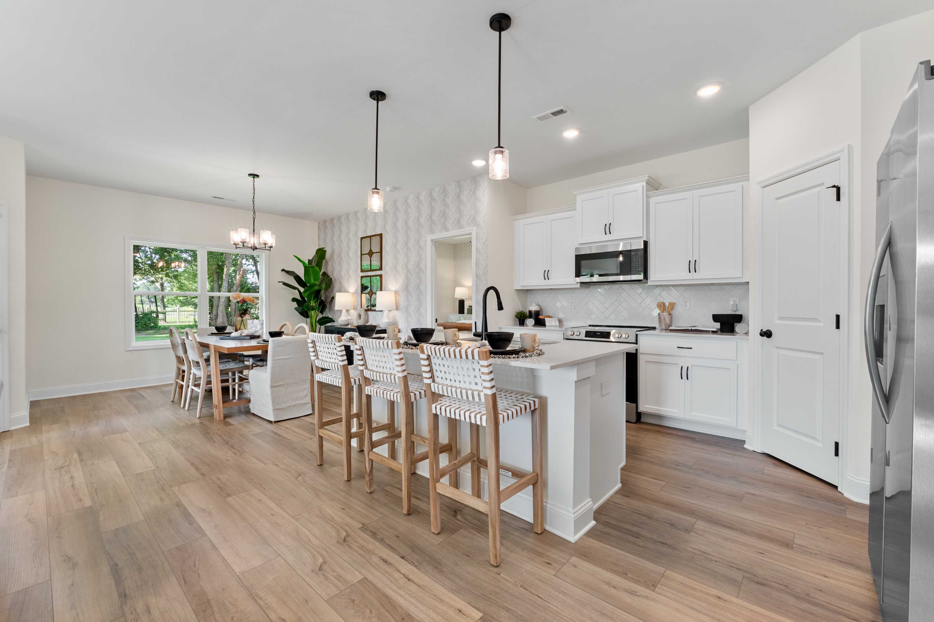 Open-concept kitchen and dining at Lynn Meadows in Meridianville AL with white cabinets, large island, bar stools, and hardwood floors