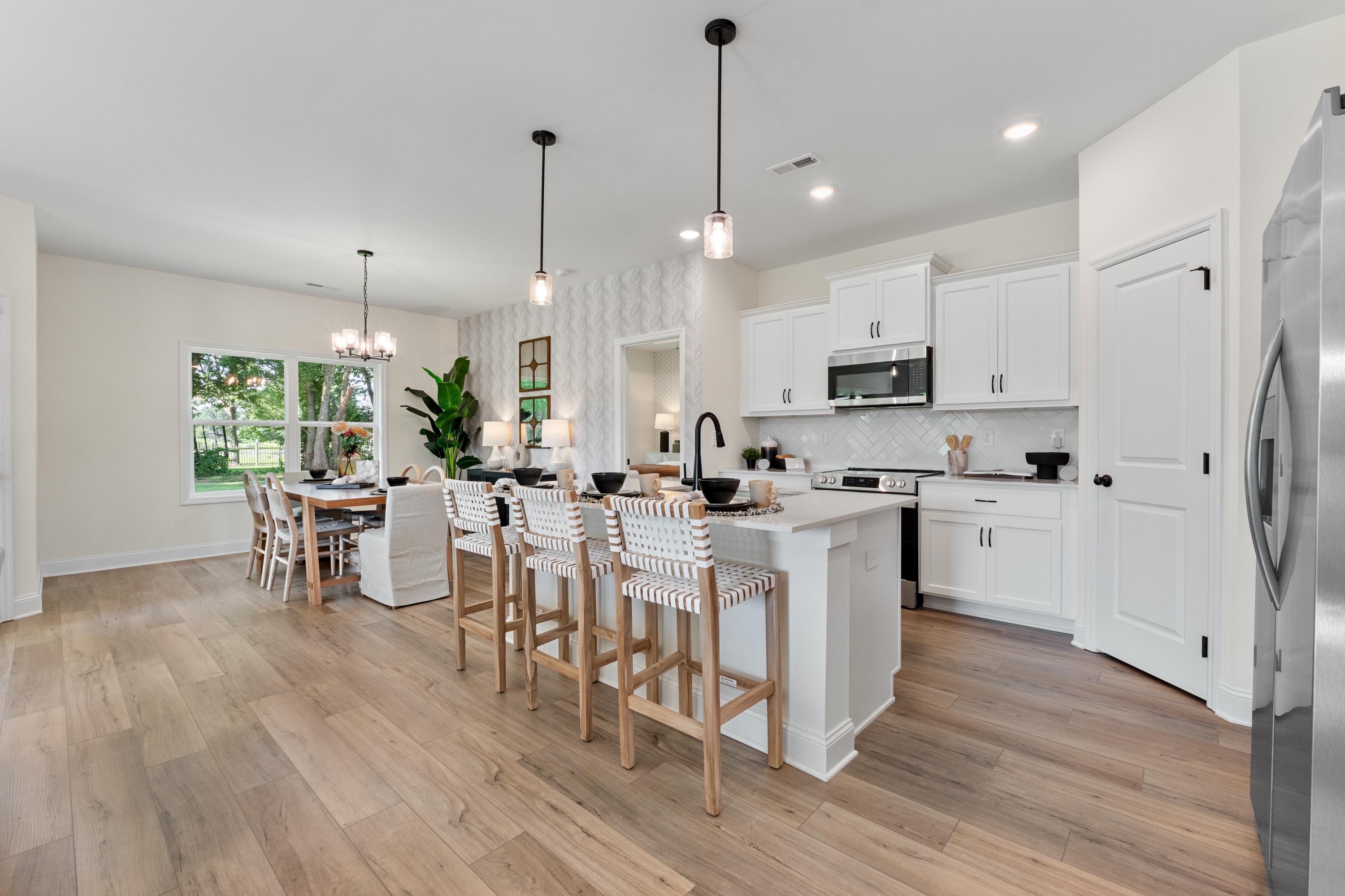 Open-concept kitchen and dining at Lynn Meadows in Meridianville AL with white cabinets, large island, bar stools, and hardwood floors