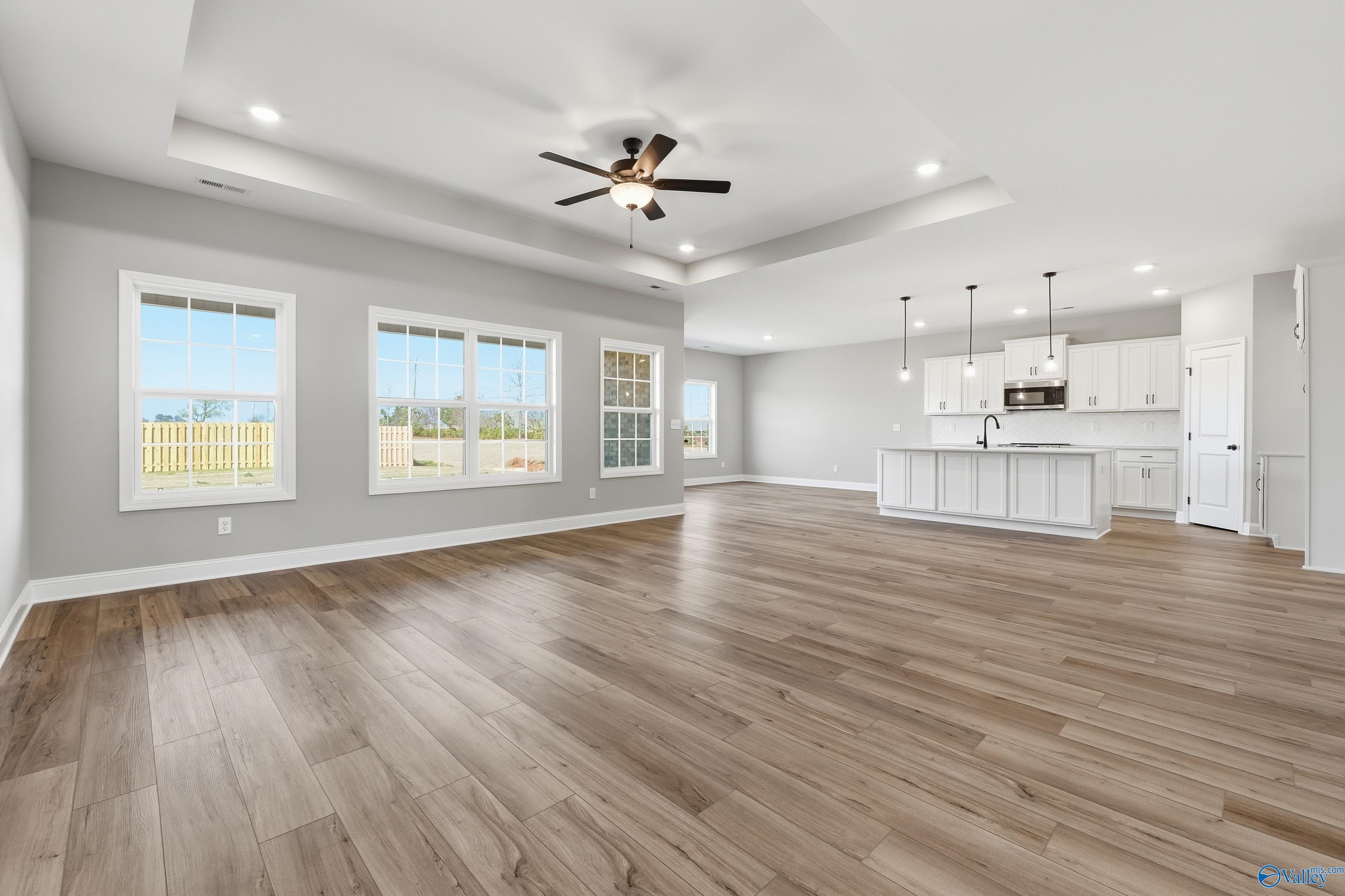 Open-concept kitchen and living area with hardwood floors, white cabinets, ceiling fan, and large windows in Davidson Homes The Rockford, Harvest, Alabama