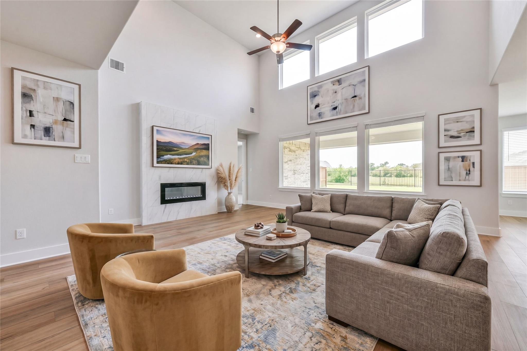 Spacious living room with beige L-shaped sofa, gold velvet swivel chairs, linear fireplace, abstract art, and large windows in Davidson Homes The Victoria A, Lago Mar, Texas City