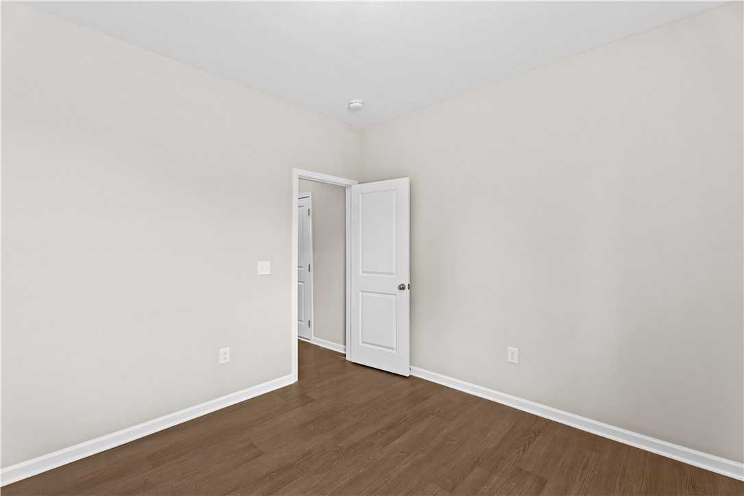 Bright bedroom with beige walls, hardwood floors, and open door to adjacent bath in The Orion 4-bedroom home, Cusseta, Alabama