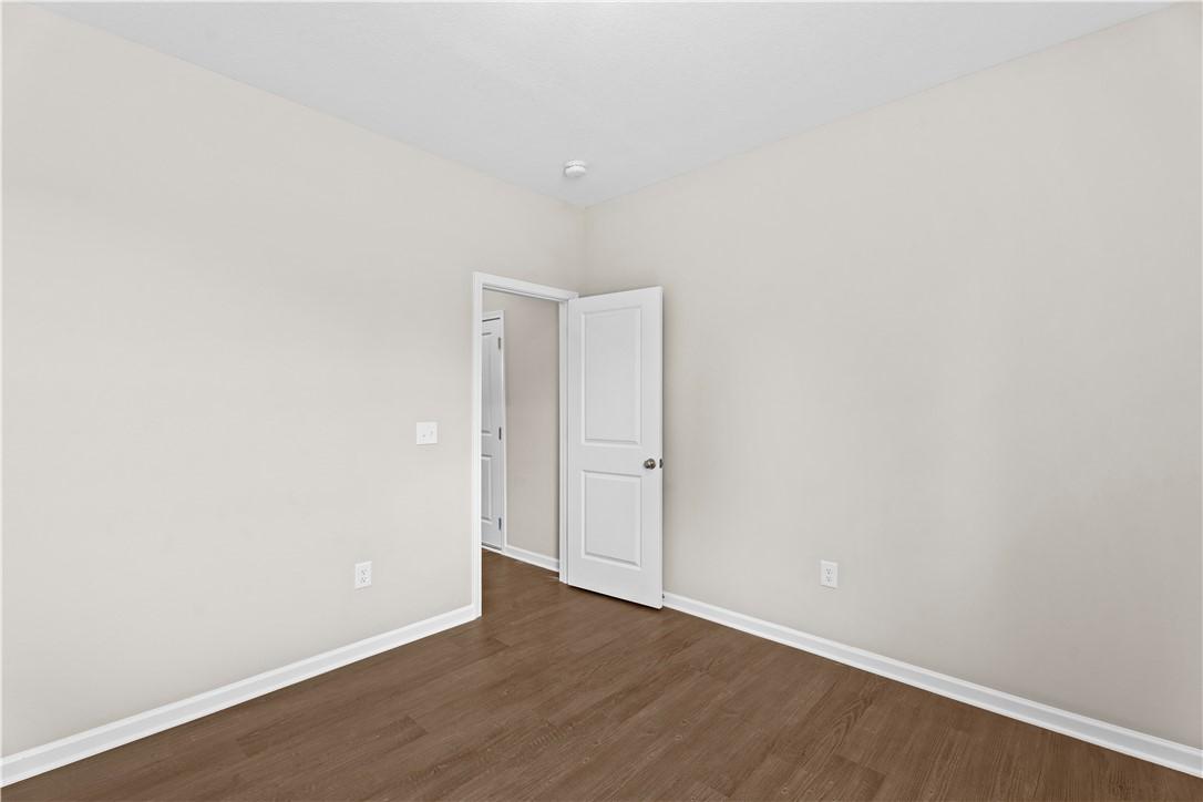 Empty bedroom with beige walls, hardwood floors, and open white door in Evermore Homes The Orion, Cusseta, Alabama