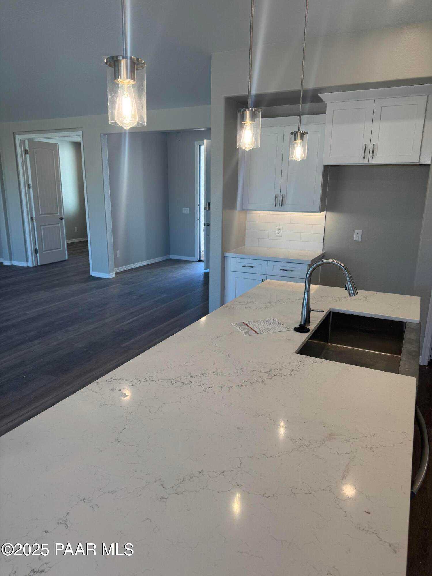 Modern open-concept kitchen with white quartz island, pendant lights, and white cabinets in The Monarch E, Prescott AZ