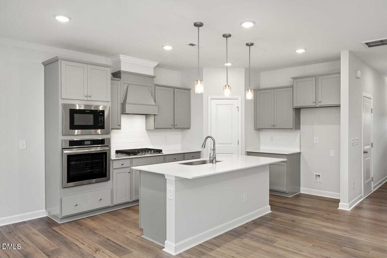 Modern white kitchen with shaker cabinets, stainless appliances, center island, and pendant lights in Davidson Homes The Warren plan, Fuquay-Varina, NC