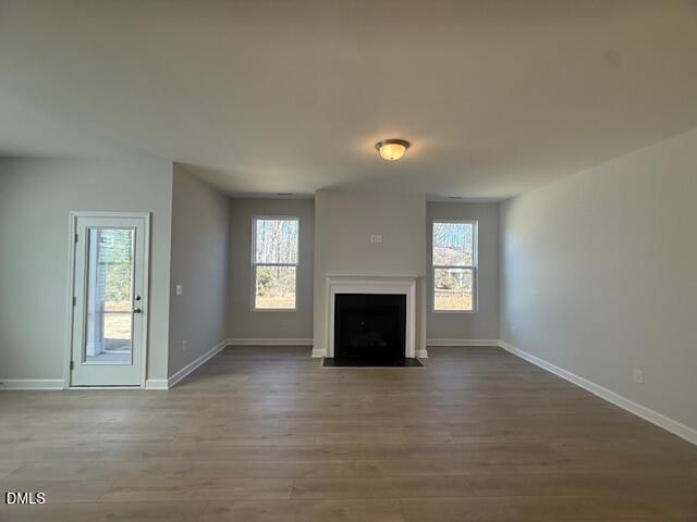 Bright living room with white stone fireplace, large windows overlooking woods, and hardwood floors in The Daphne C, Zebulon, NC