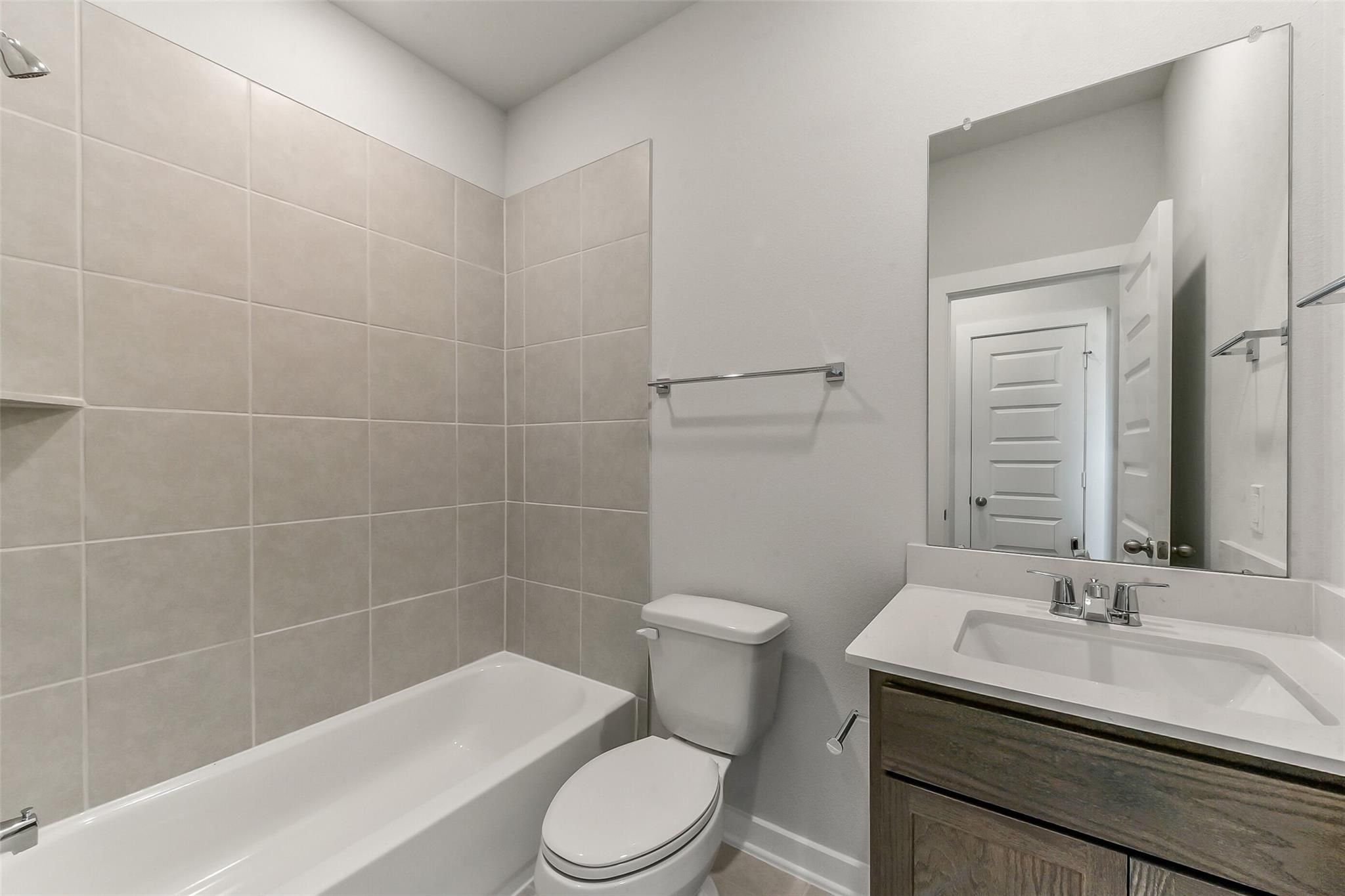 Modern bathroom featuring tiled shower, bathtub, white toilet, and oak vanity in Davidson Homes The Sabine F, Dayton, Texas