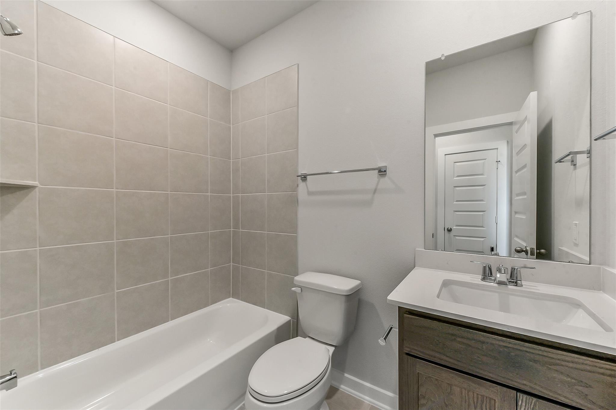 Modern bathroom featuring tiled shower, bathtub, white toilet, and oak vanity in Davidson Homes The Sabine F, Dayton, Texas
